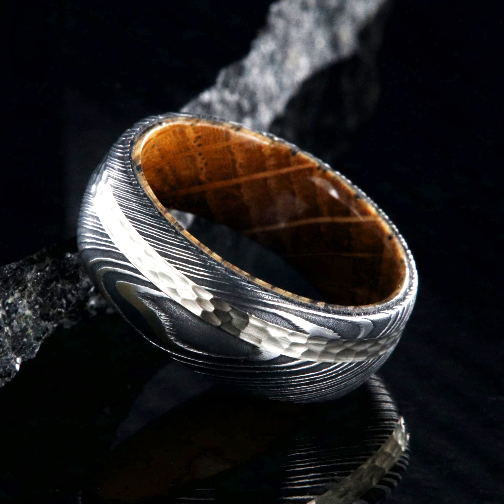 8mm wide black Damascus steel ring with a 2mm wide hammered white gold inlay and a whiskey barrel sleeve