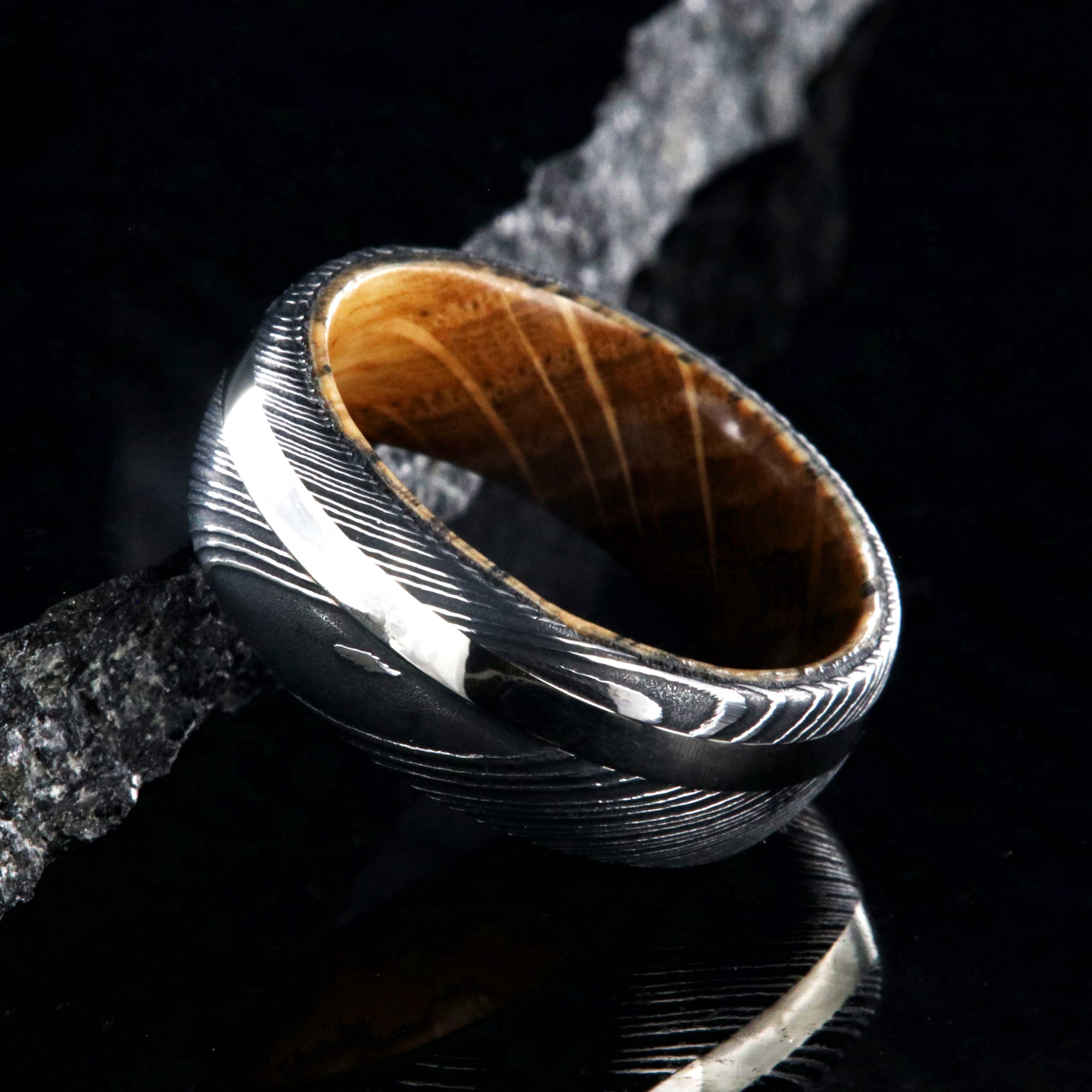 8mm wide mens ring with black Damascus steel and a wide gold off-center inlay and a Jack Daniels whiskey barrel sleeve