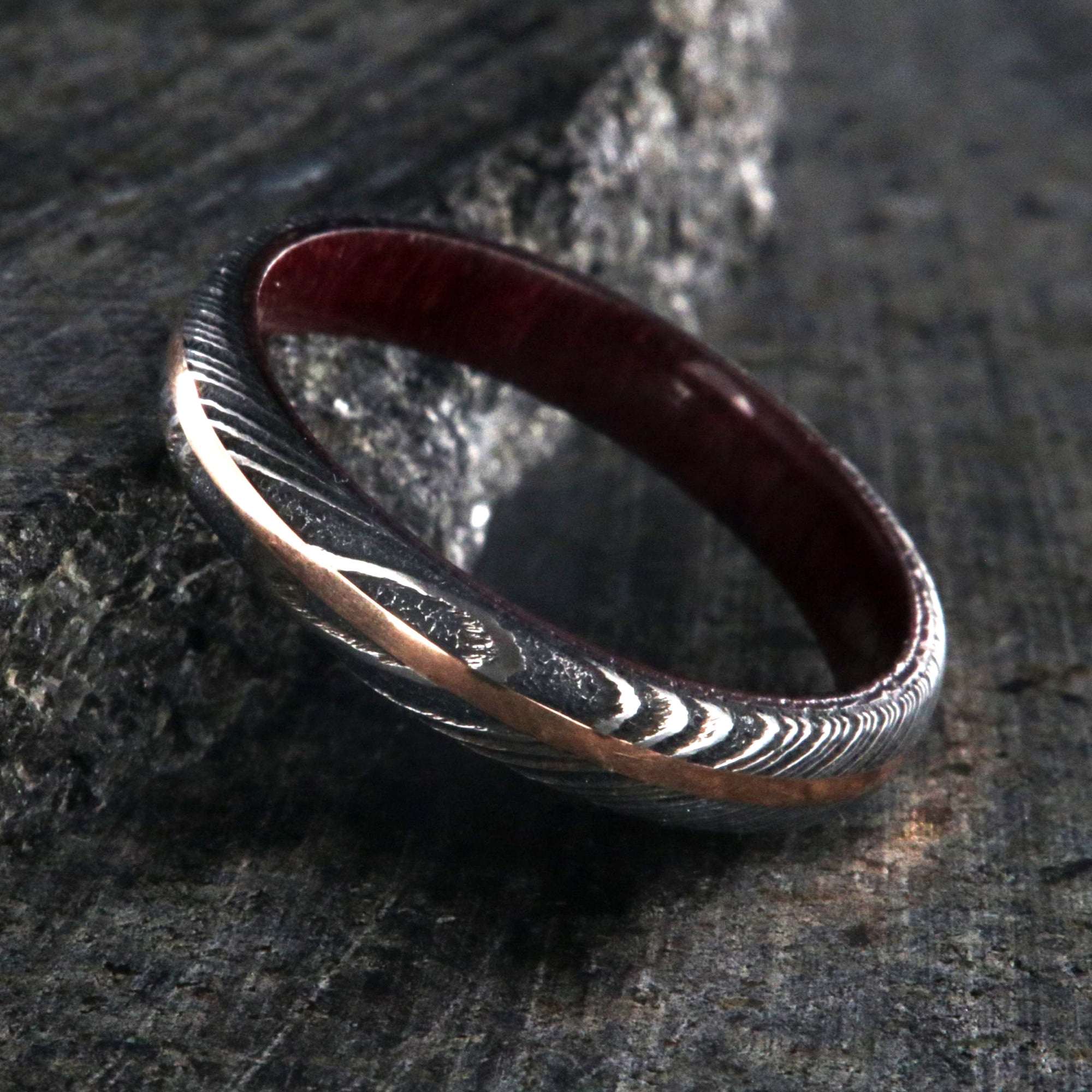 4mm wide women's wedding band made with black Damascus steel with a centered rose gold inlay and purple rain wood sleeve