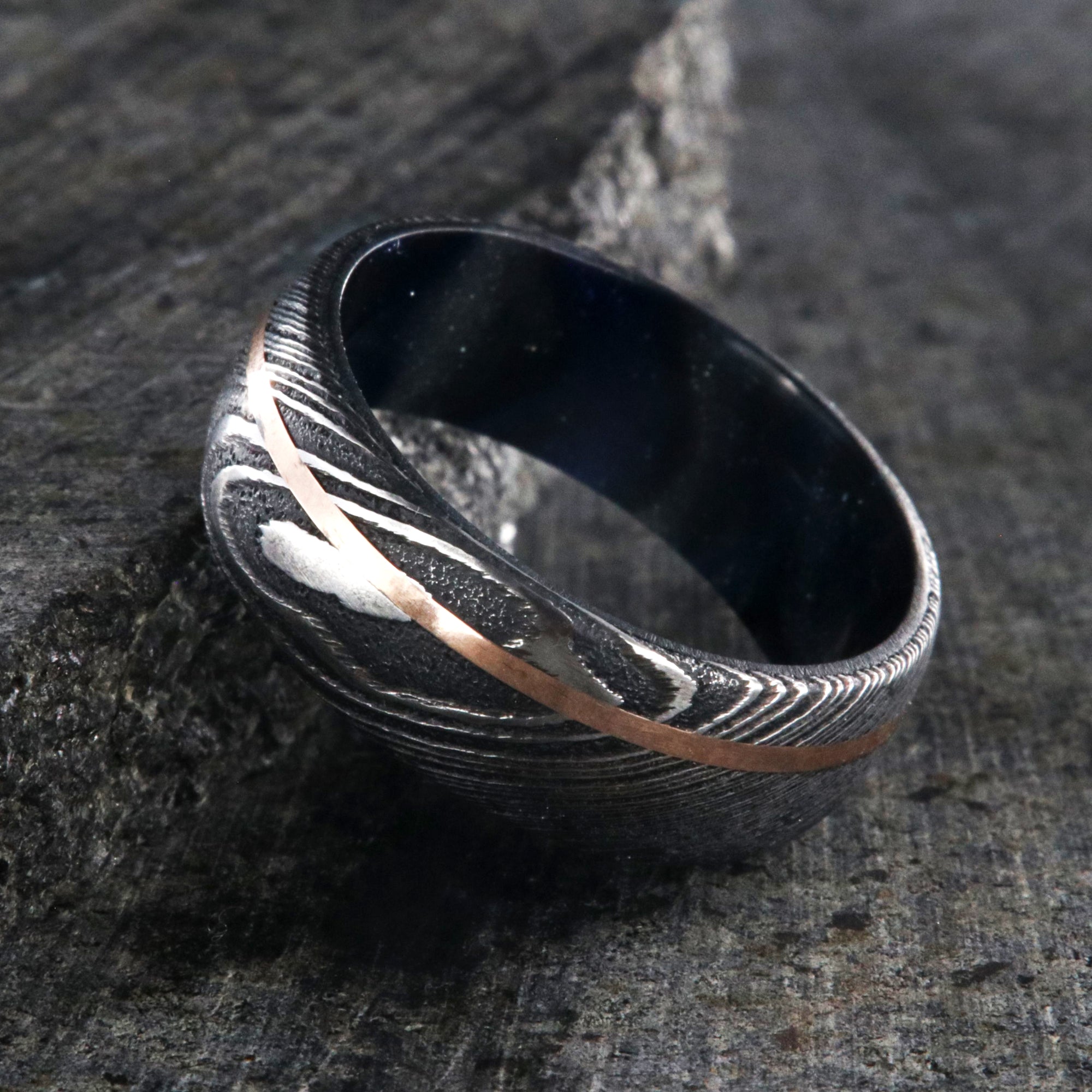 8mm wide Damascus steel wedding band with a thin rose gold off-center inlay and glittering blue and silver sleeve