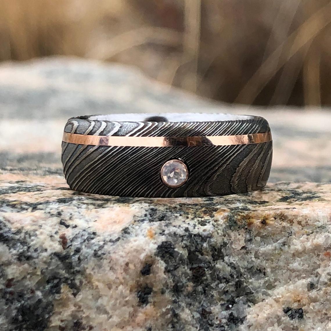 8mm wide black Damascus steel wedding band with an off-centered rose gold inlay with a 3mm round diamond