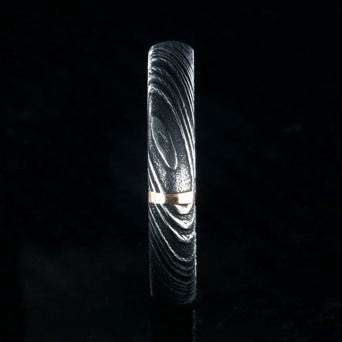 4mm wide black Damascus steel wedding band with a single vertical rose gold inlay