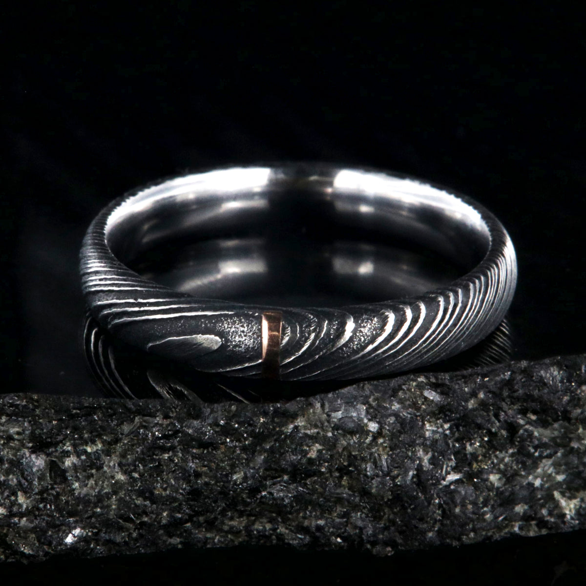 4mm wide black Damascus steel wedding band with a single vertical rose gold inlay