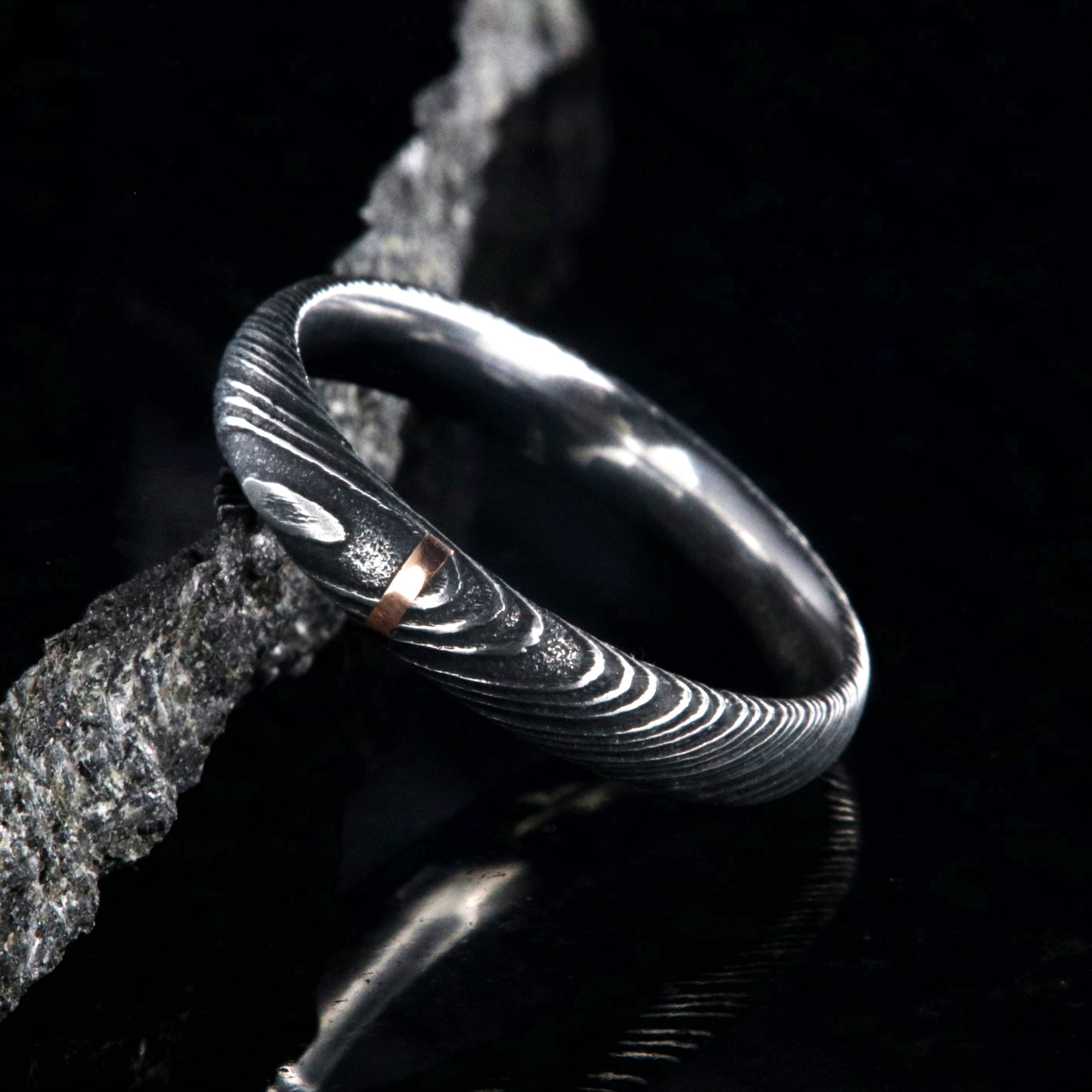 4mm wide black Damascus steel wedding band with a single vertical rose gold inlay