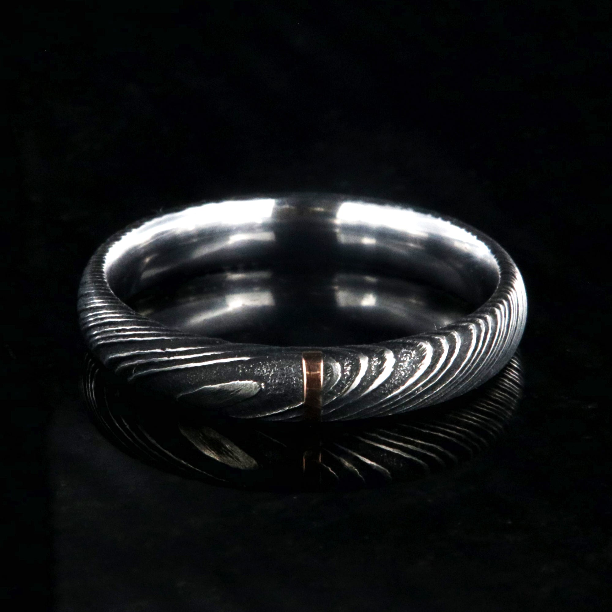 4mm wide black Damascus steel wedding band with a single vertical rose gold inlay