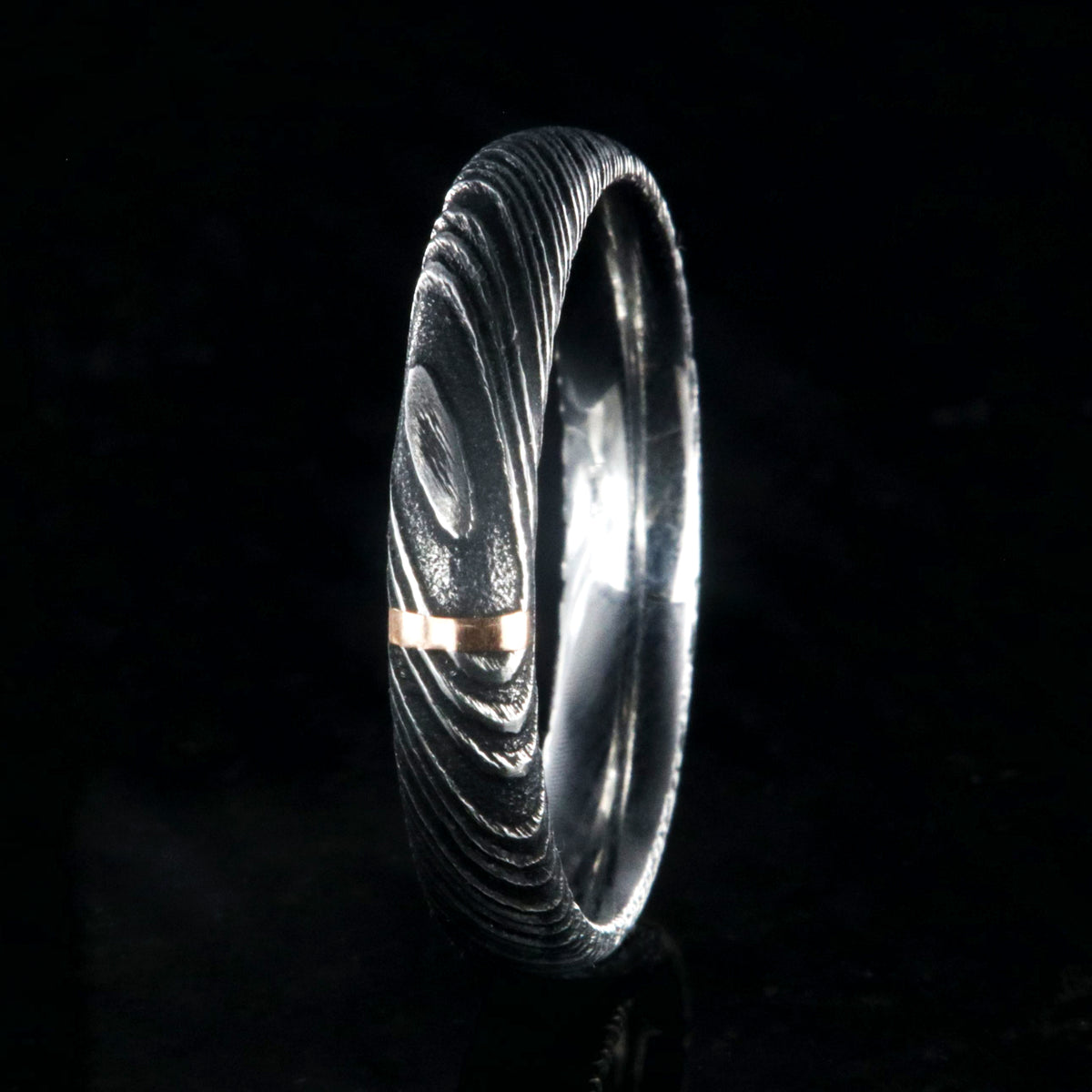 4mm wide black Damascus steel wedding band with a single vertical rose gold inlay