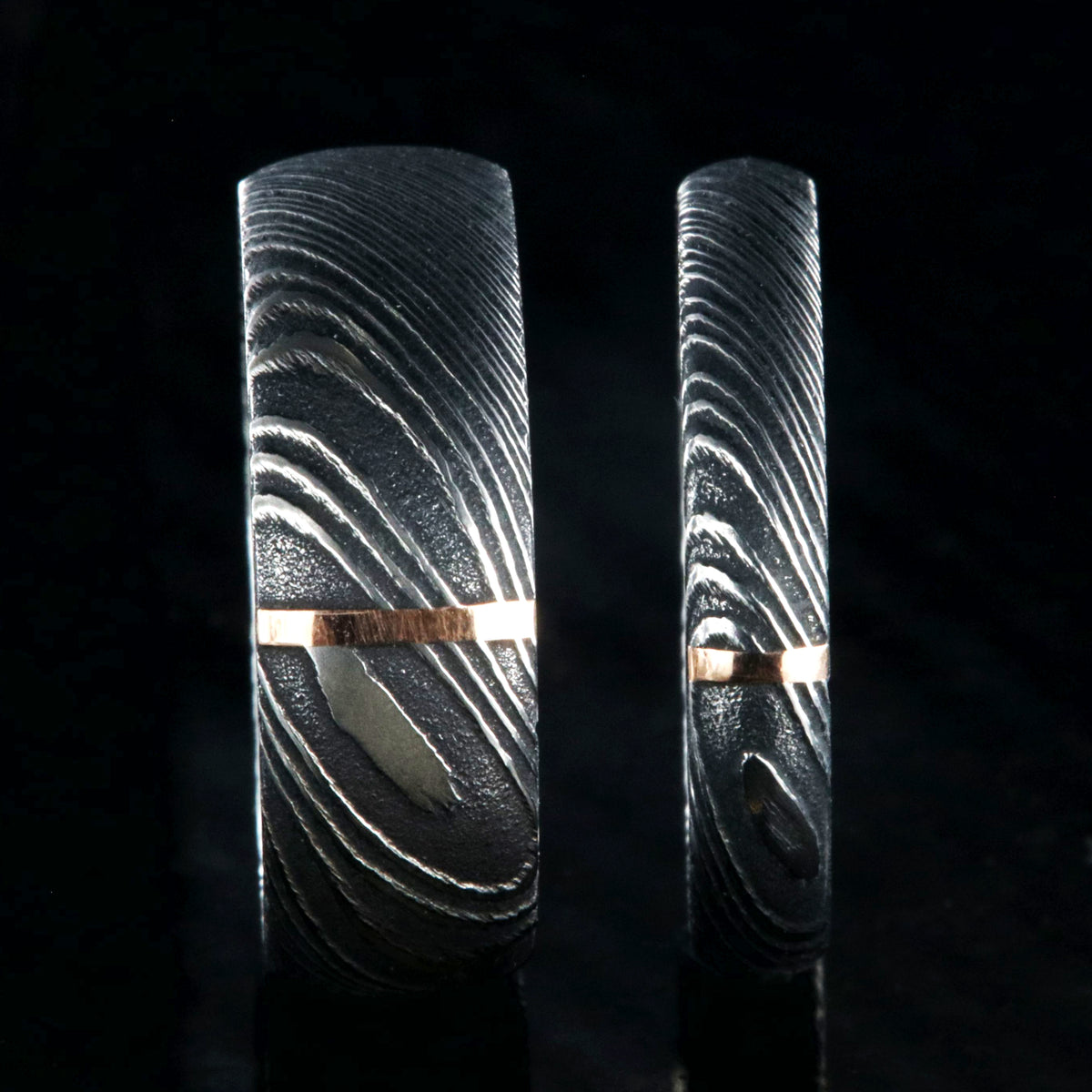A matching black Damascus steel wedding band set with 8mm and 4mm wide rings and a single vertical rose gold inlay