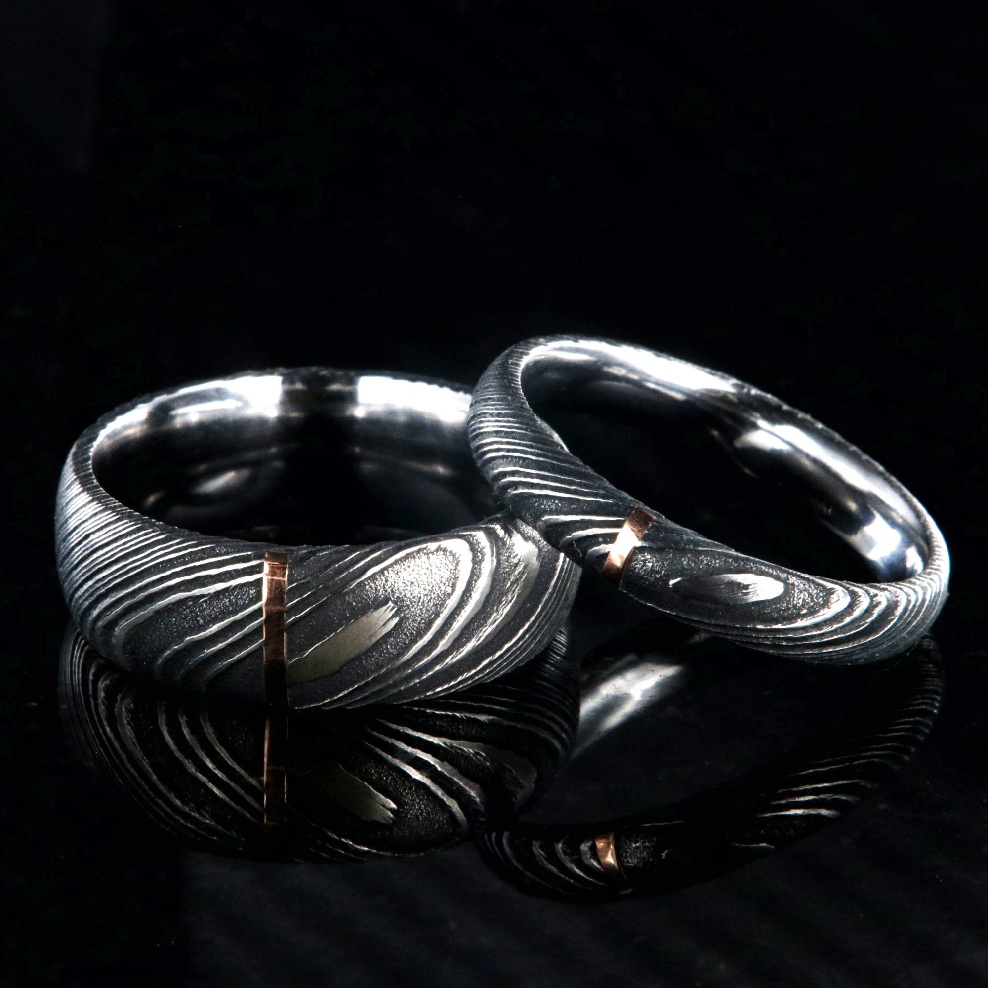 A matching black Damascus steel wedding band set with 8mm and 4mm wide rings and a single vertical rose gold inlay