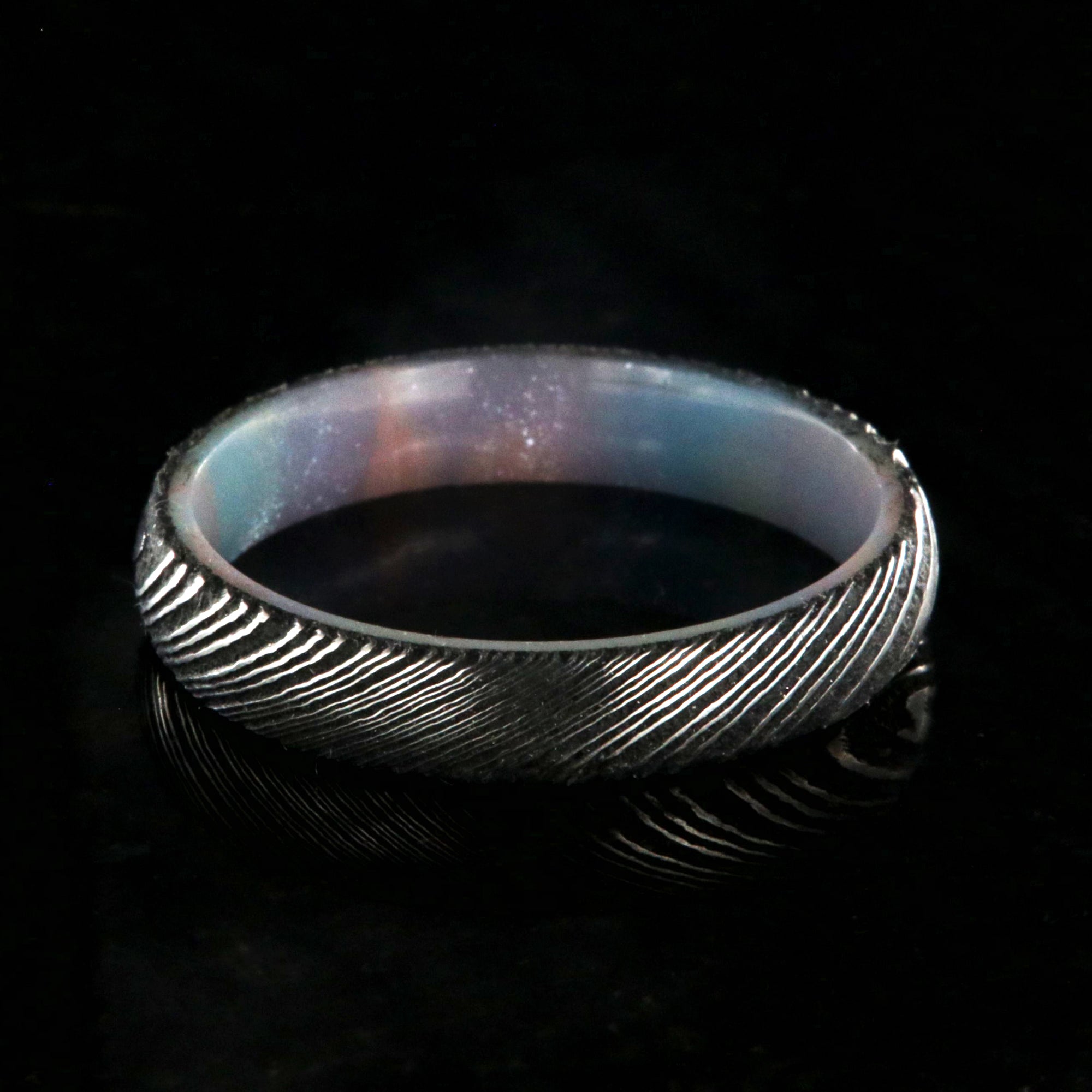 4mm wide black Damascus steel ring with a rounded profile and a glittering rainbow sleeve