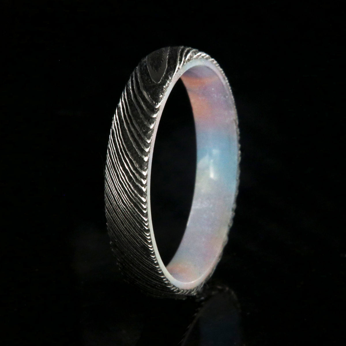 4mm wide black Damascus steel ring with a rounded profile and a glittering rainbow sleeve