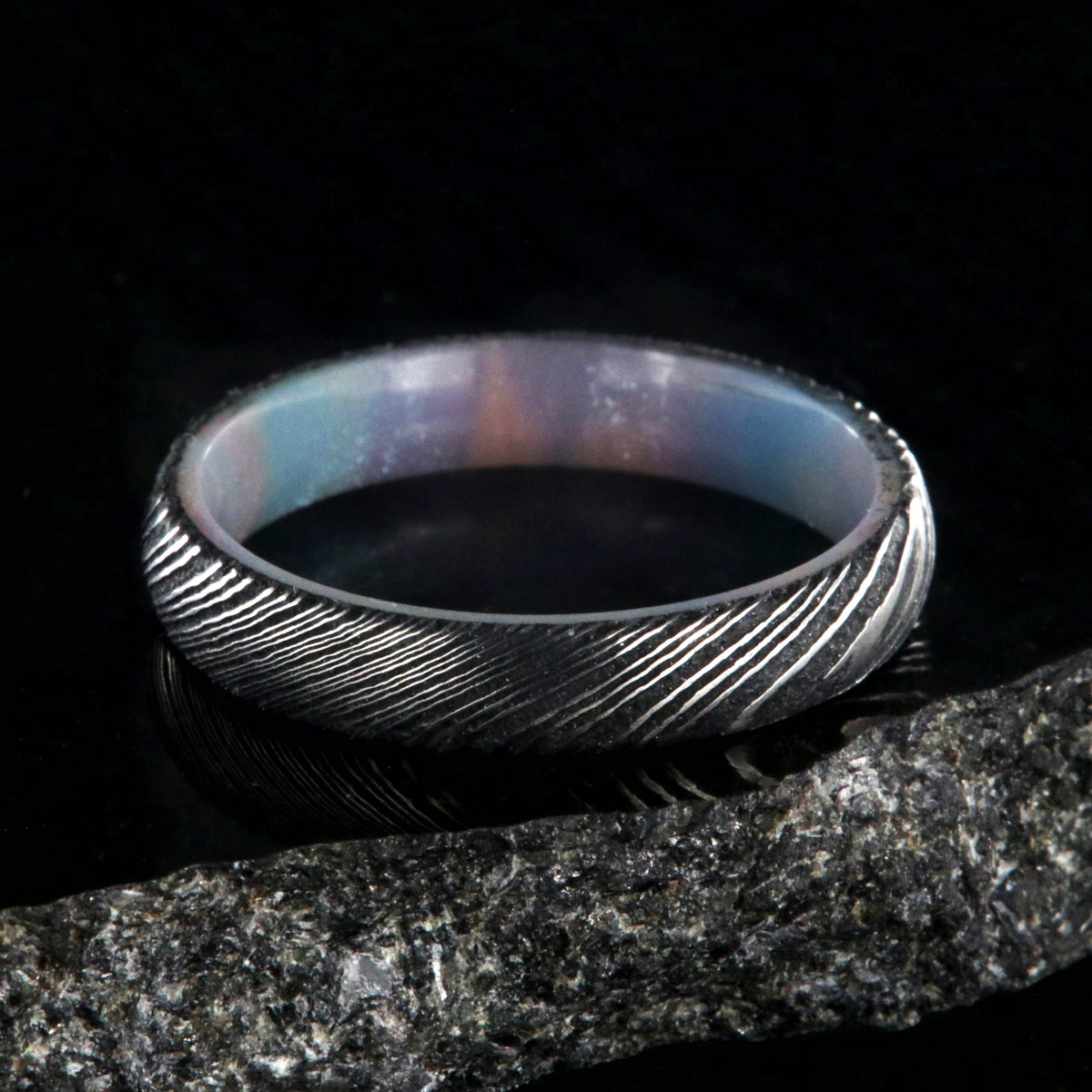 4mm wide black Damascus steel ring with a rounded profile and a glittering rainbow sleeve