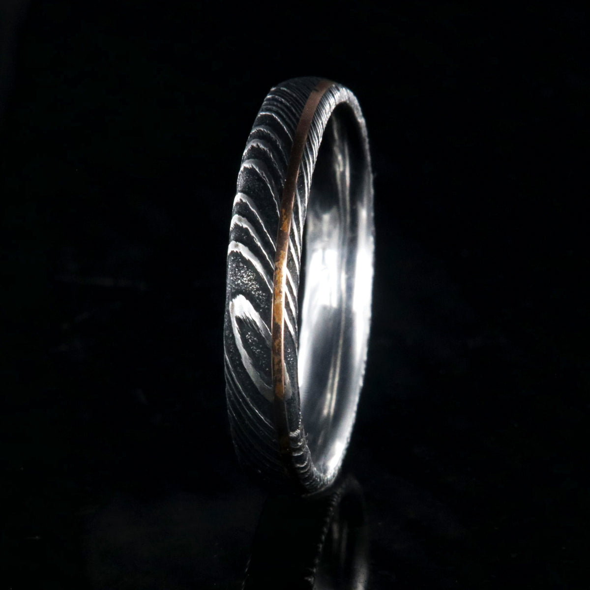 4mm wide black Damascus steel ring with ultra thin rose gold off-center inlay with polished inside