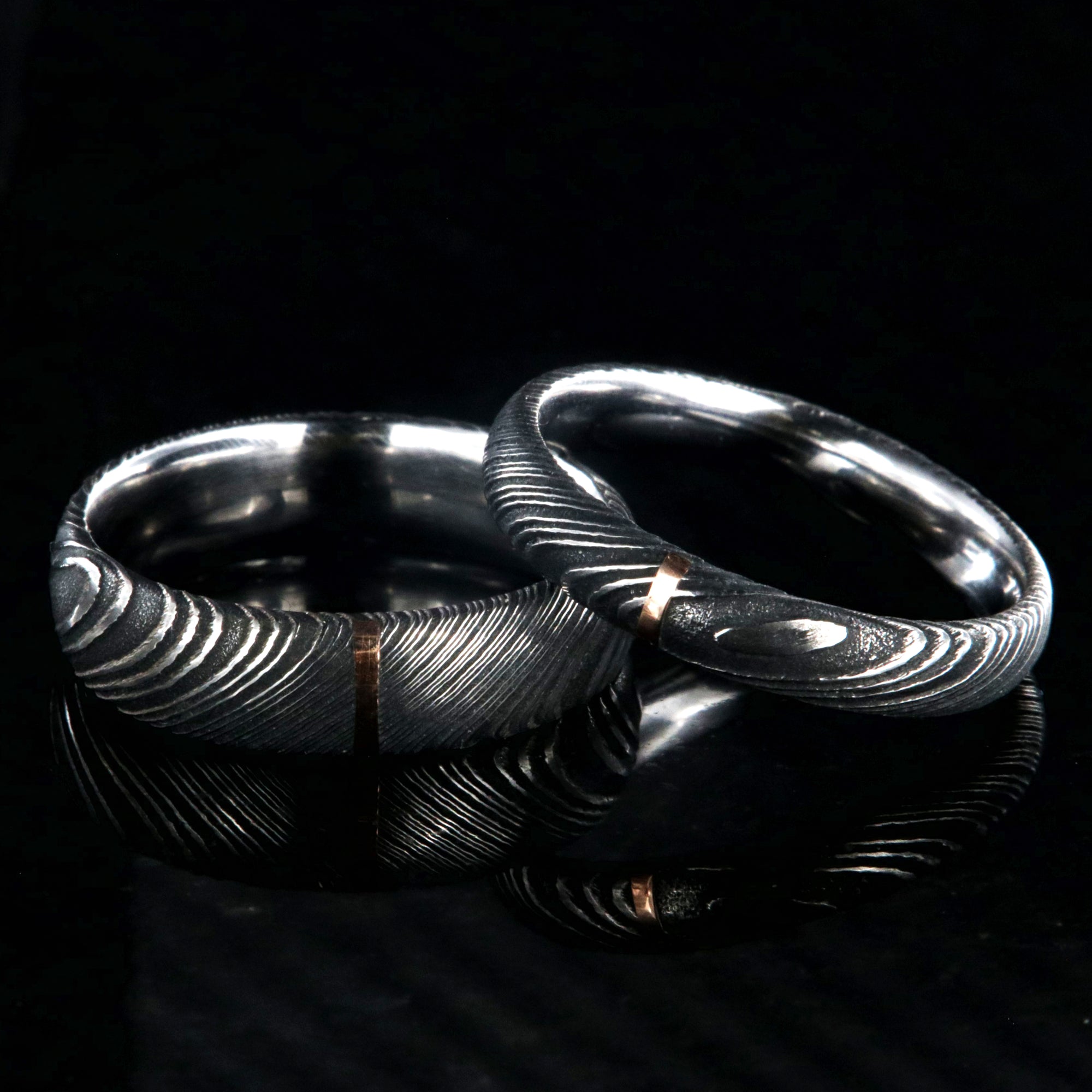 A matching set of Damascus steel wedding ring with a 6mm and 4mm wide bands with a single vertical rose gold inlay