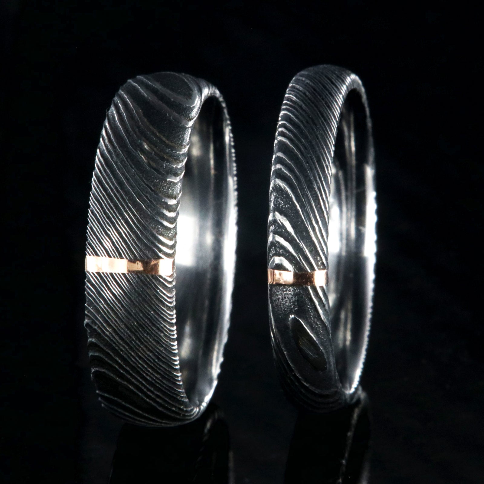 A matching set of Damascus steel wedding ring with a 6mm and 4mm wide bands with a single vertical rose gold inlay