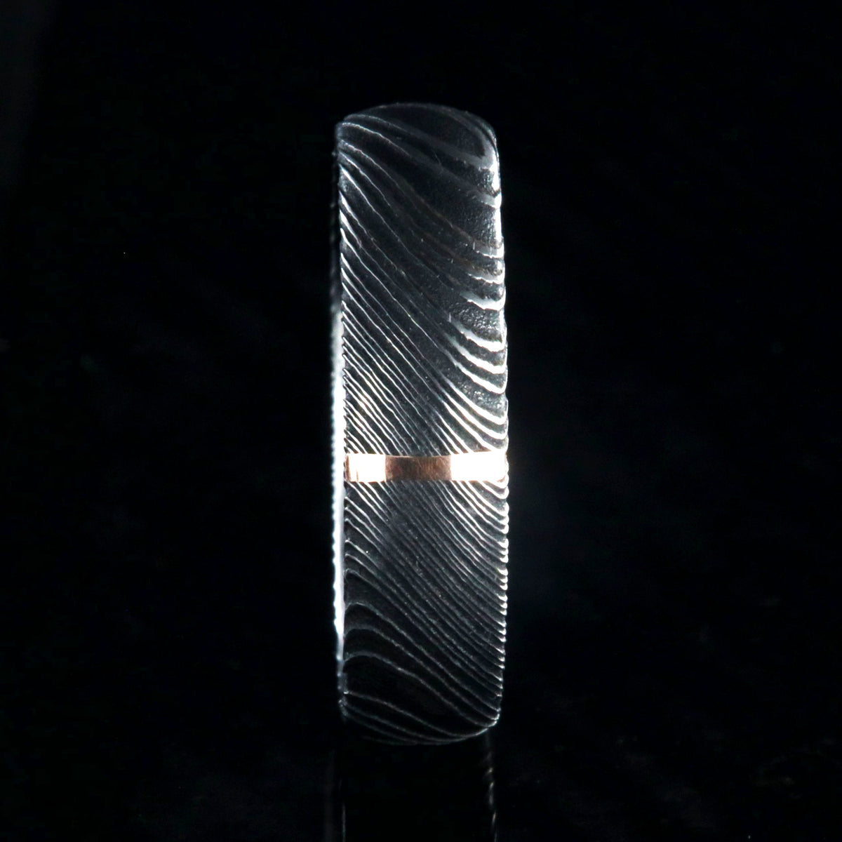 6mm wide black Damascus steel wedding band with a single vertical rose gold inlay