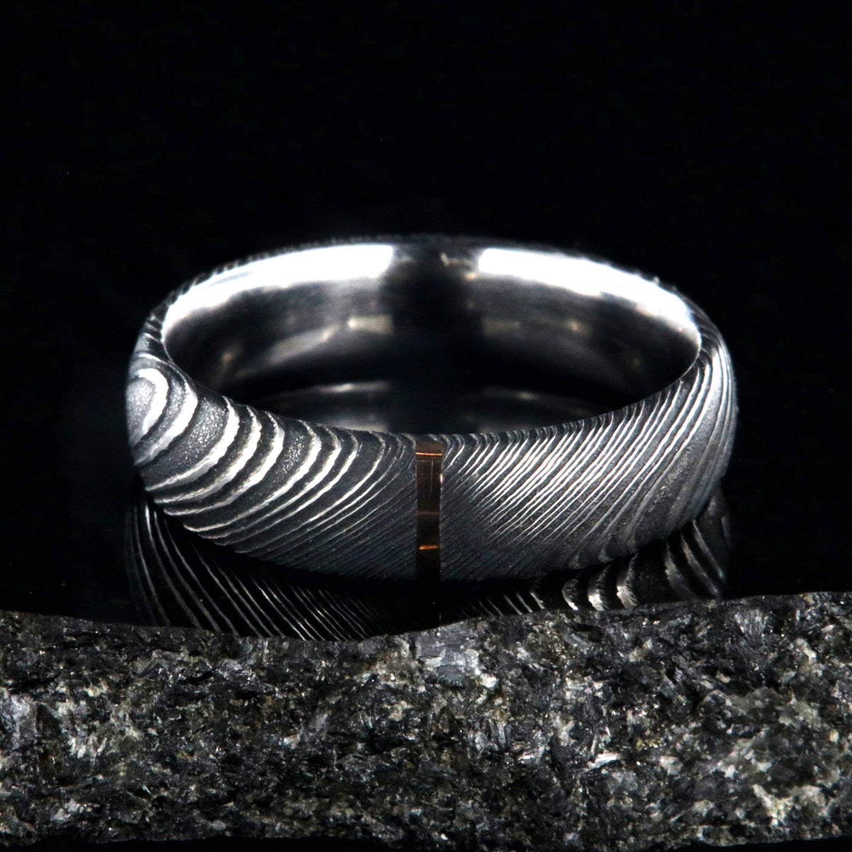 6mm wide black Damascus steel wedding band with a single vertical rose gold inlay