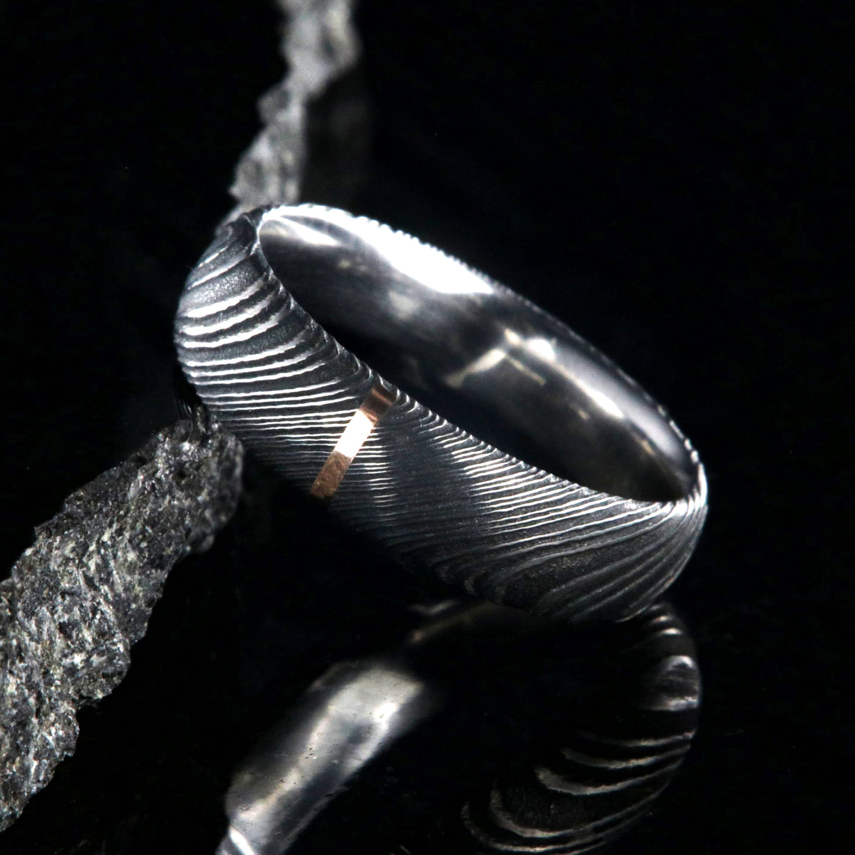 6mm wide black Damascus steel wedding band with a single vertical rose gold inlay