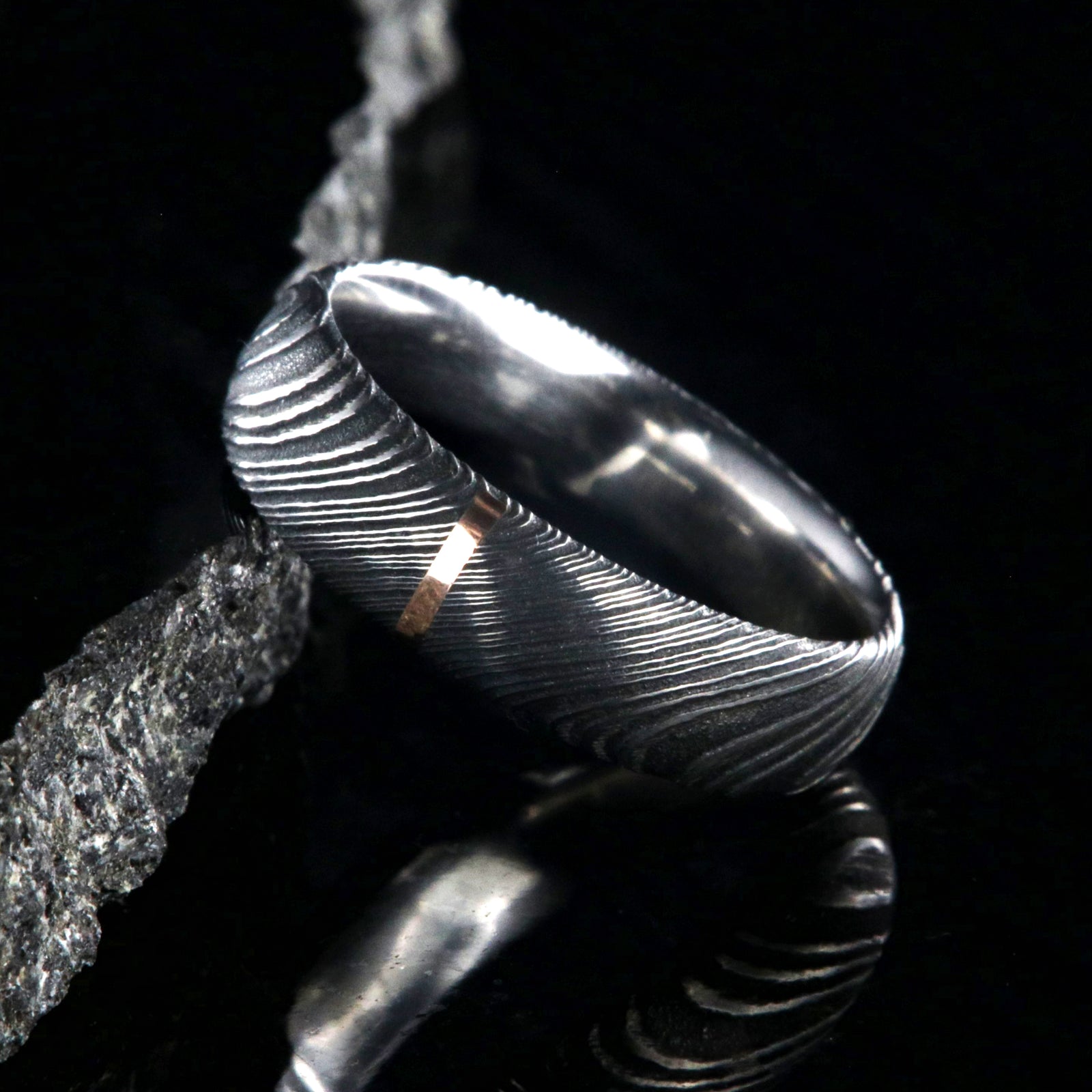 6mm wide black Damascus steel wedding band with a single vertical rose gold inlay