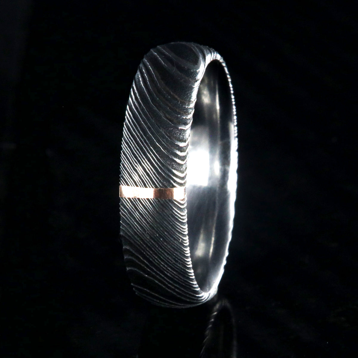 6mm wide black Damascus steel wedding band with a single vertical rose gold inlay