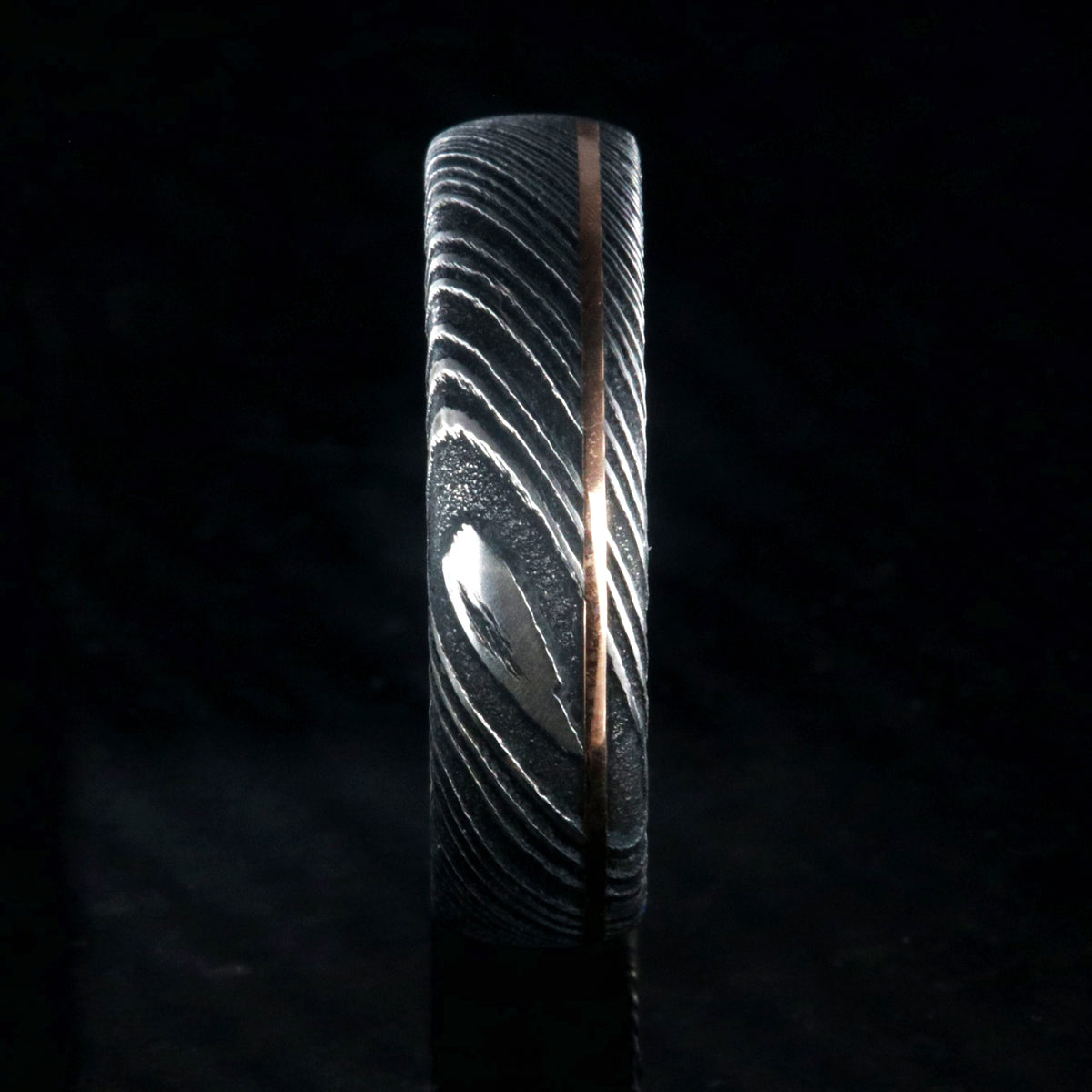 6mm wide black Damascus steel wedding band with rounded profile, polished inside, and ultra-thin off-center rose gold inlay