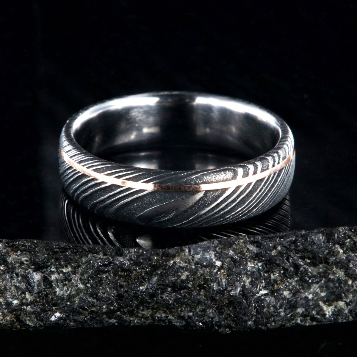 6mm wide black Damascus steel wedding band with rounded profile, polished inside, and ultra-thin off-center rose gold inlay