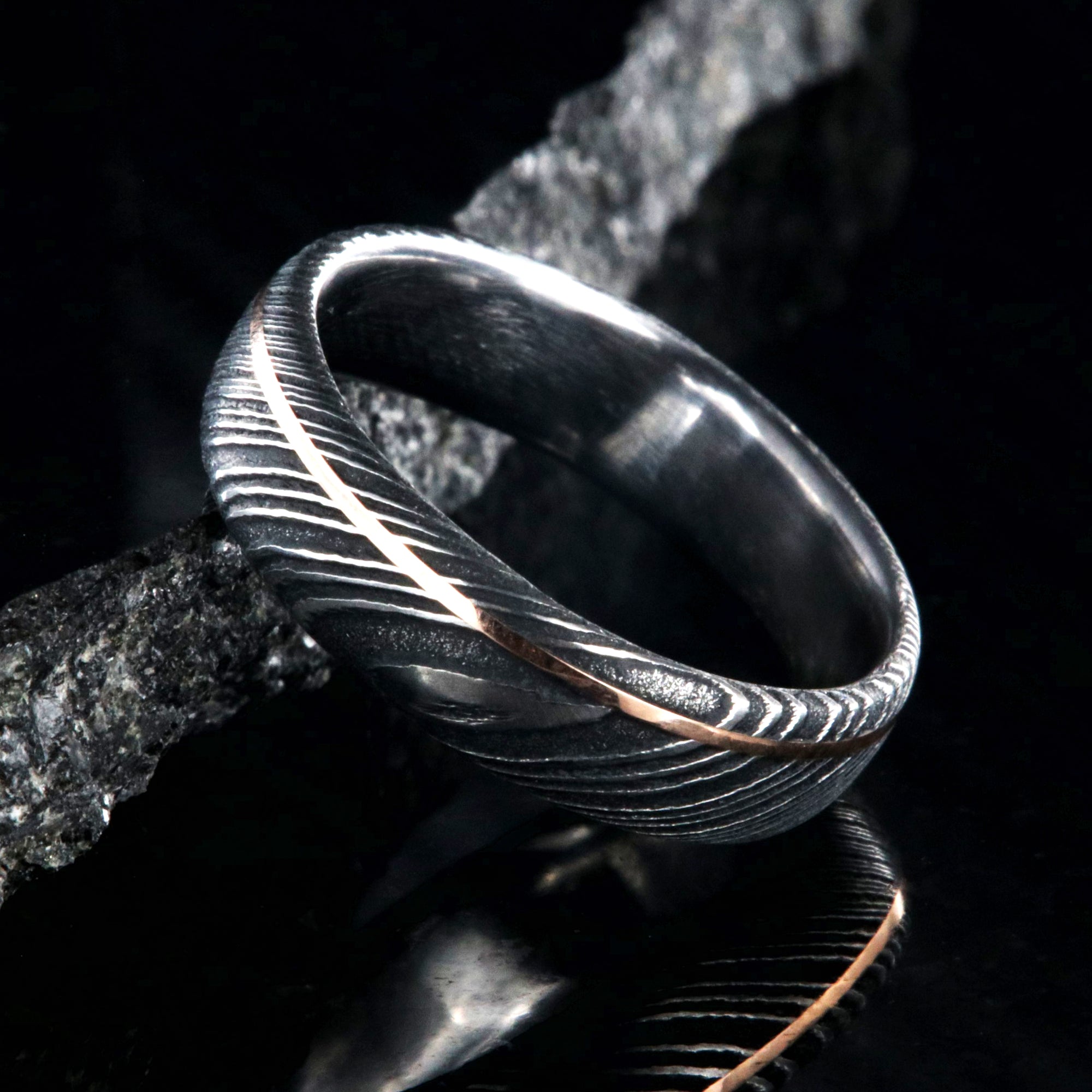 6mm wide black Damascus steel wedding band with rounded profile, polished inside, and ultra-thin off-center rose gold inlay