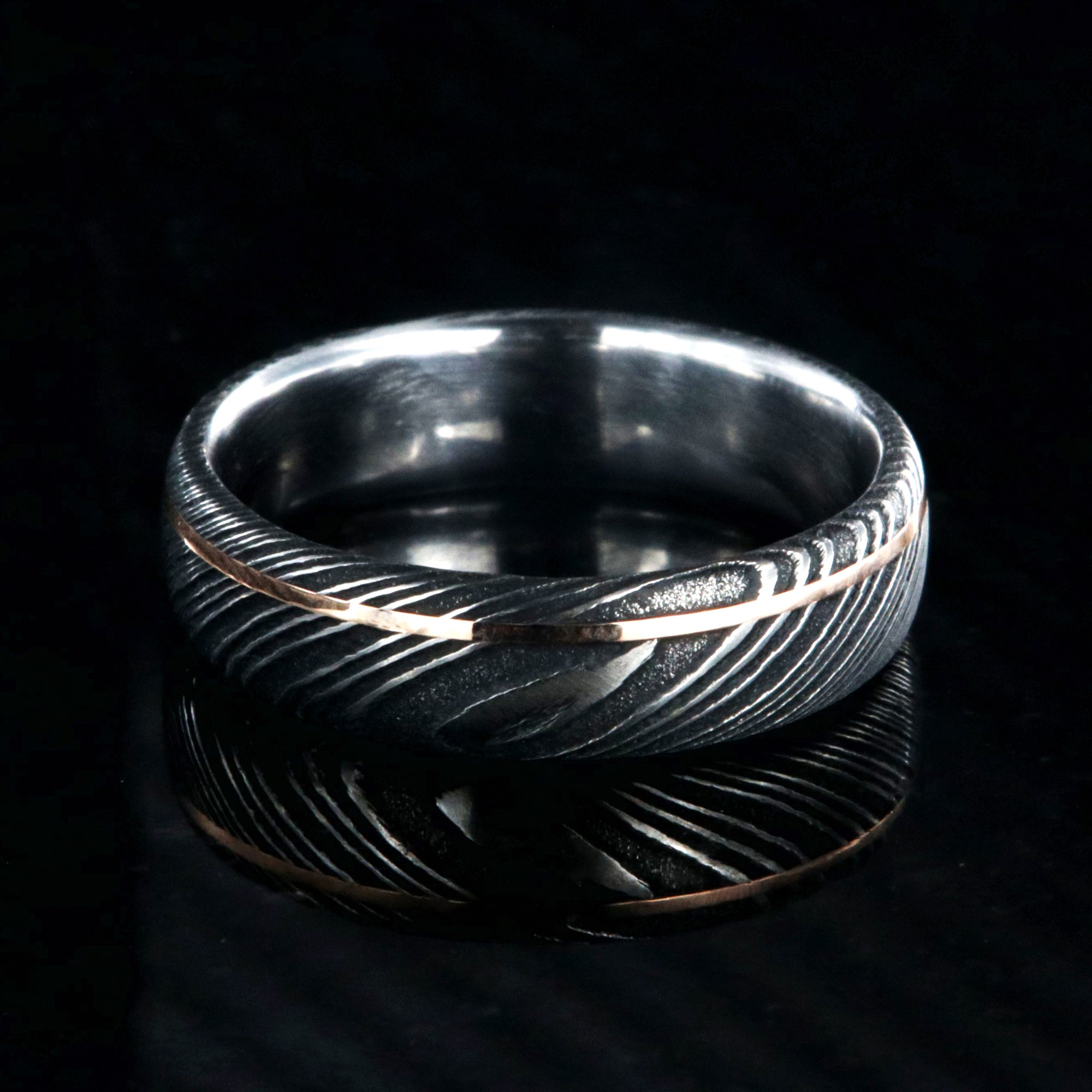 6mm wide black Damascus steel wedding band with rounded profile, polished inside, and ultra-thin off-center rose gold inlay