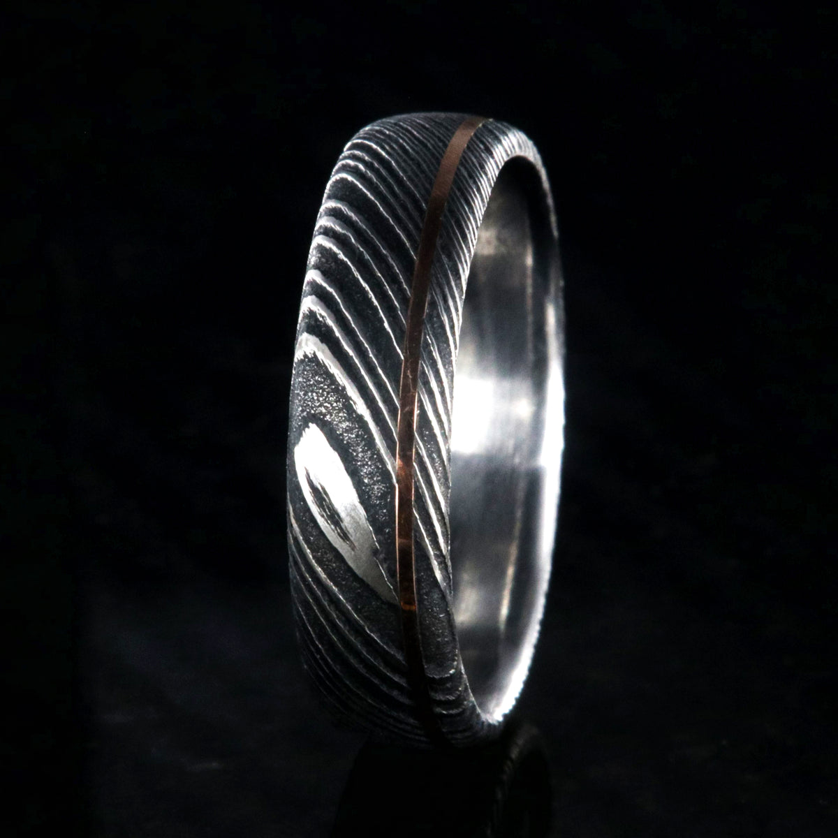 6mm wide black Damascus steel wedding band with rounded profile, polished inside, and ultra-thin off-center rose gold inlay