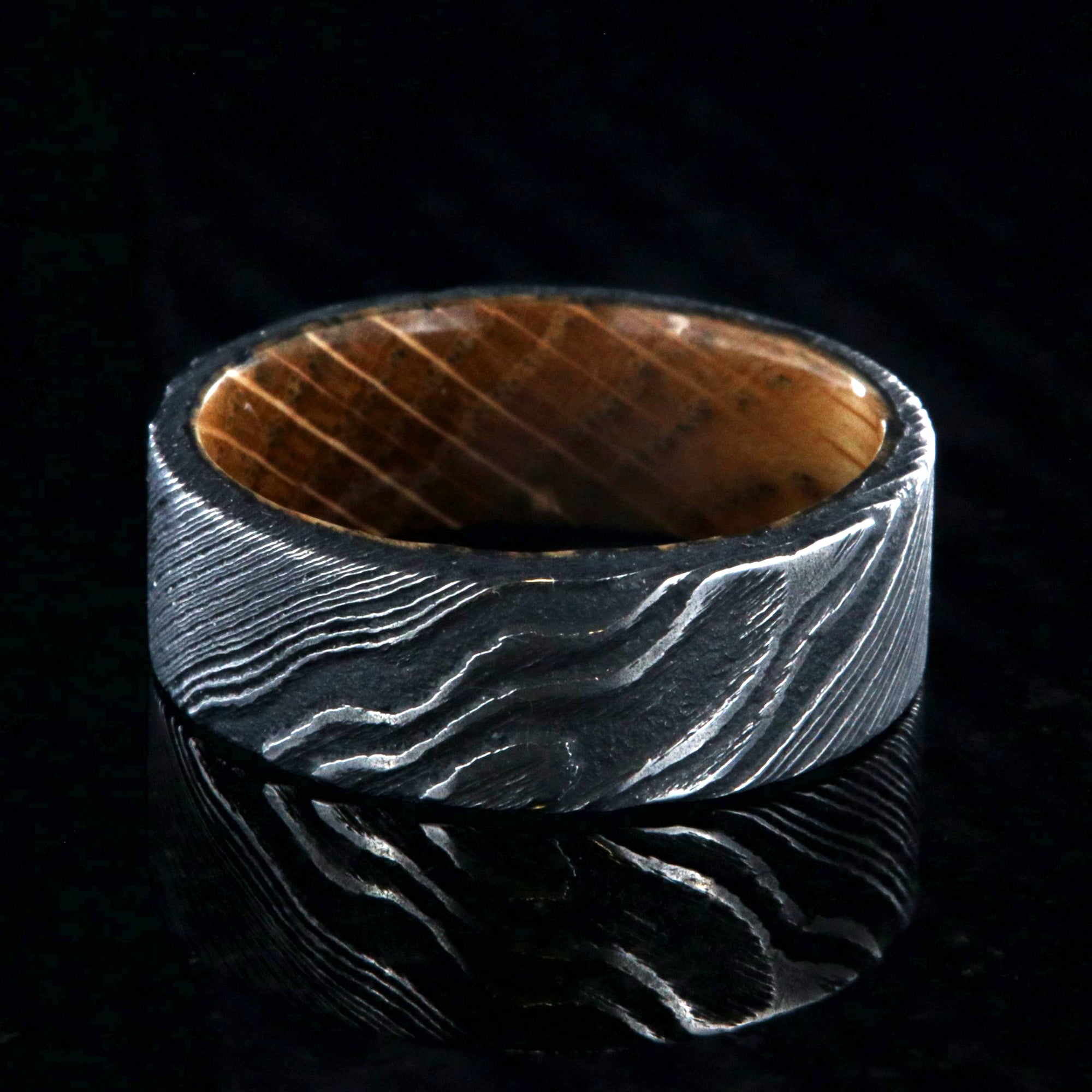 8mm wide black Damascus steel ring with flat profile and a Jack Daniel's whiskey barrel sleeve