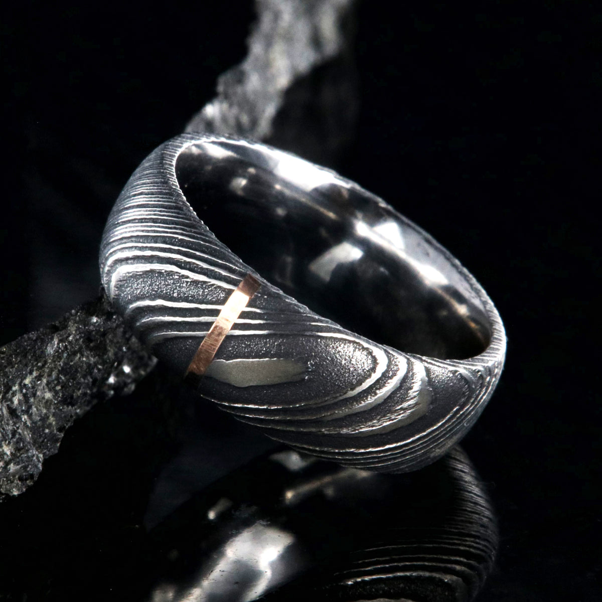8mm wide black Damascus steel wedding band with a single vertical rose gold inlay