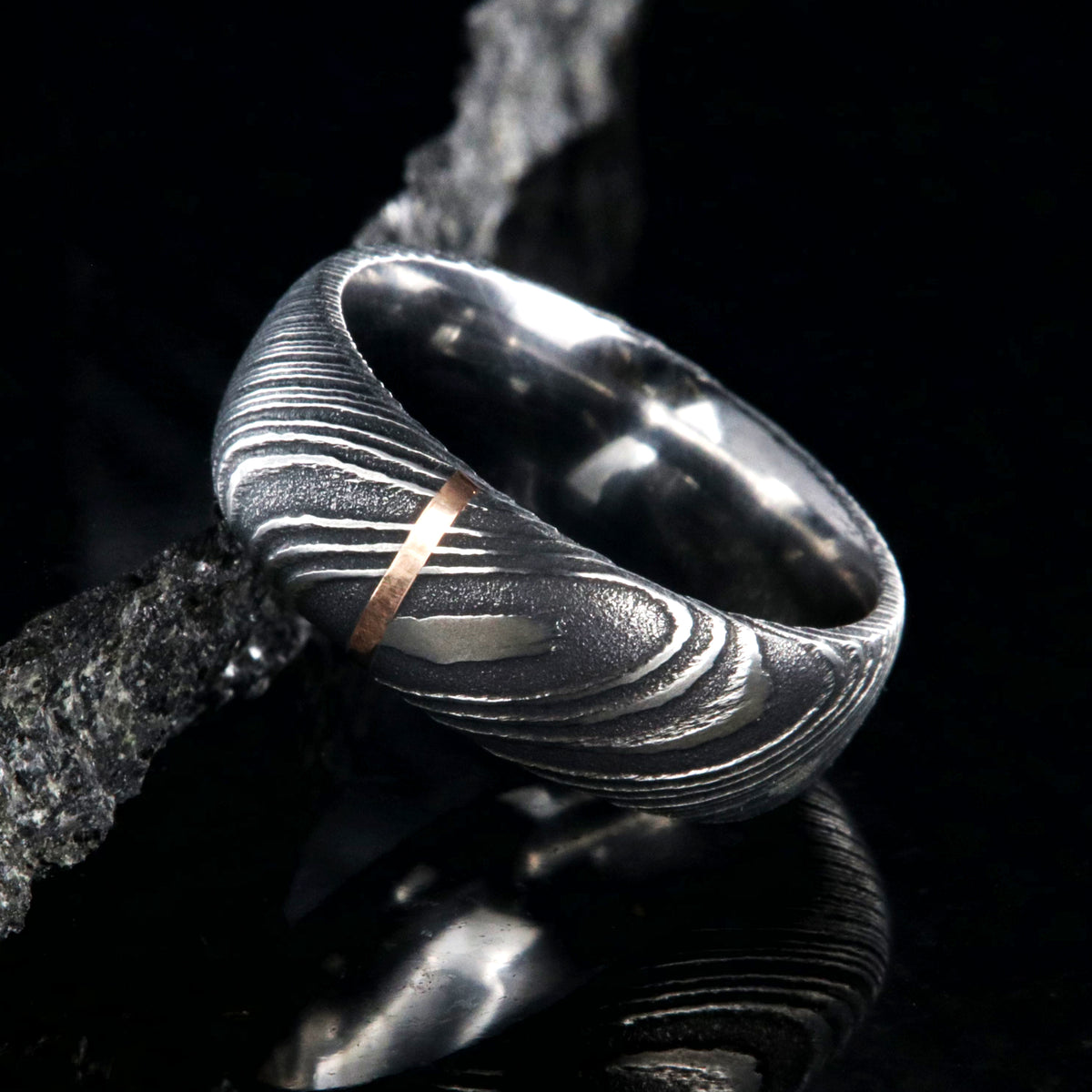 8mm wide black Damascus steel wedding band with a single vertical rose gold inlay