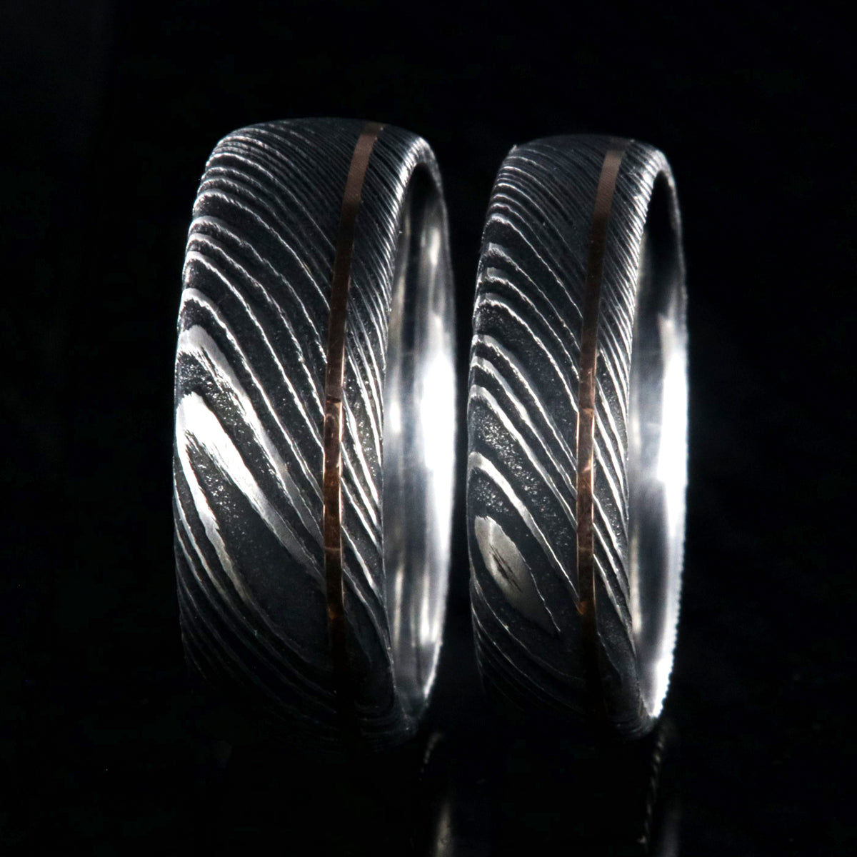8mm and 6mm wide black Damascus steel matching wedding band set with ultra-thin off-centered rose gold inlay