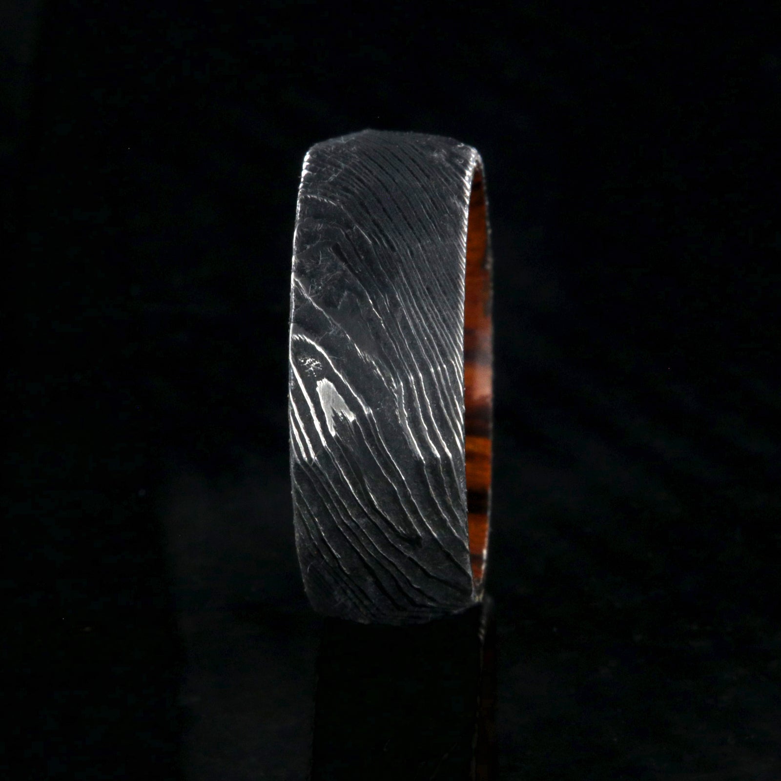 8mm wide black Damascus steel men's wedding band with an Arizona ironwood sleeve and hammered band finish