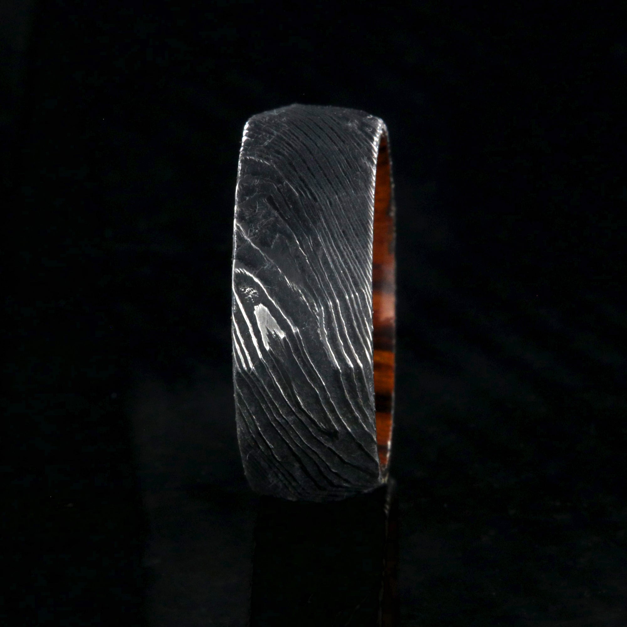 8mm wide black Damascus steel men's wedding band with an Arizona ironwood sleeve and hammered band finish
