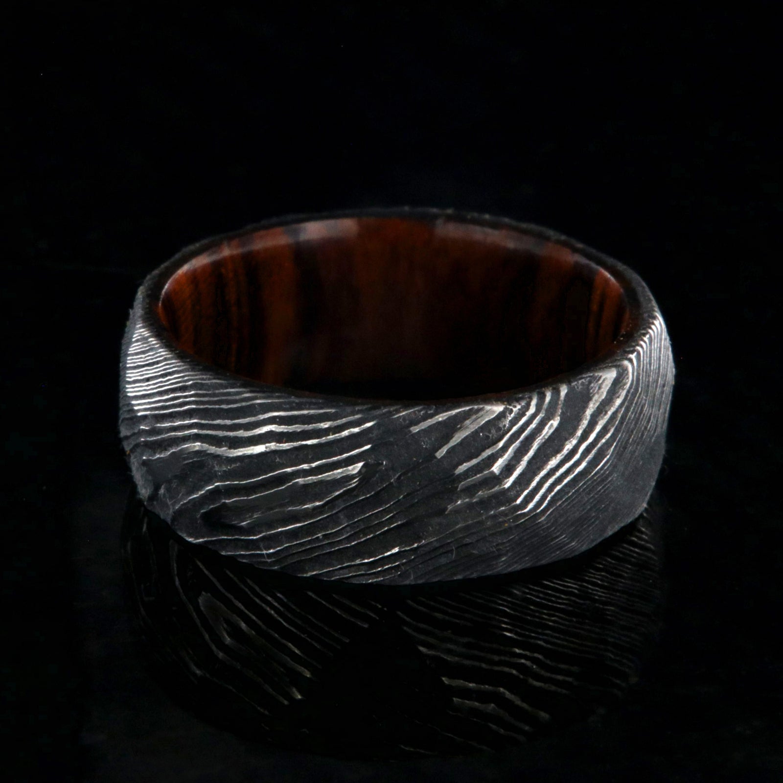 8mm wide black Damascus steel men's wedding band with an Arizona ironwood sleeve and hammered band finish