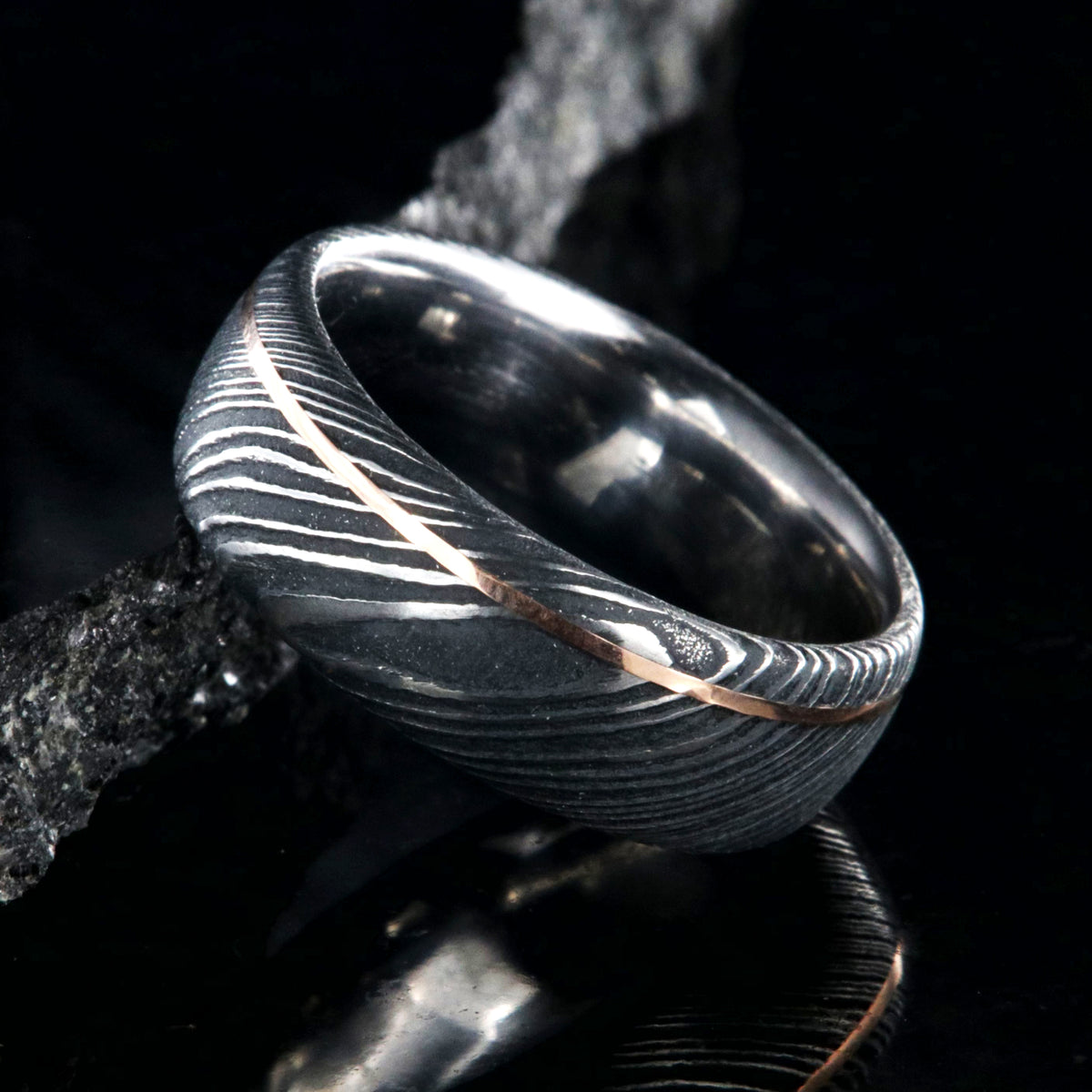 8mm wide black Damascus steel wedding band with rounded profile, polished inside, and ultra-thin off-center rose gold inlay