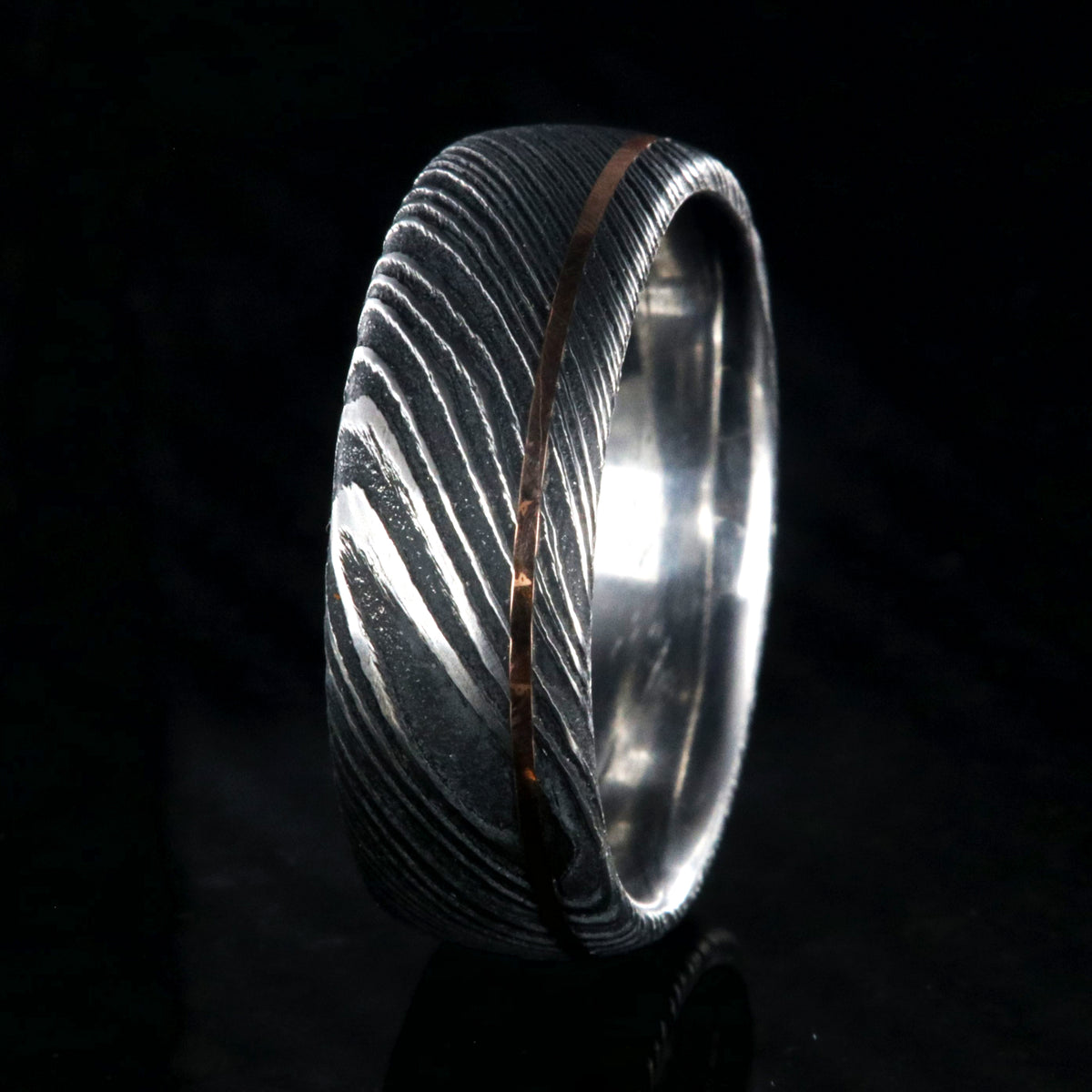 8mm wide black Damascus steel wedding band with an ultra-thin rose gold inlay