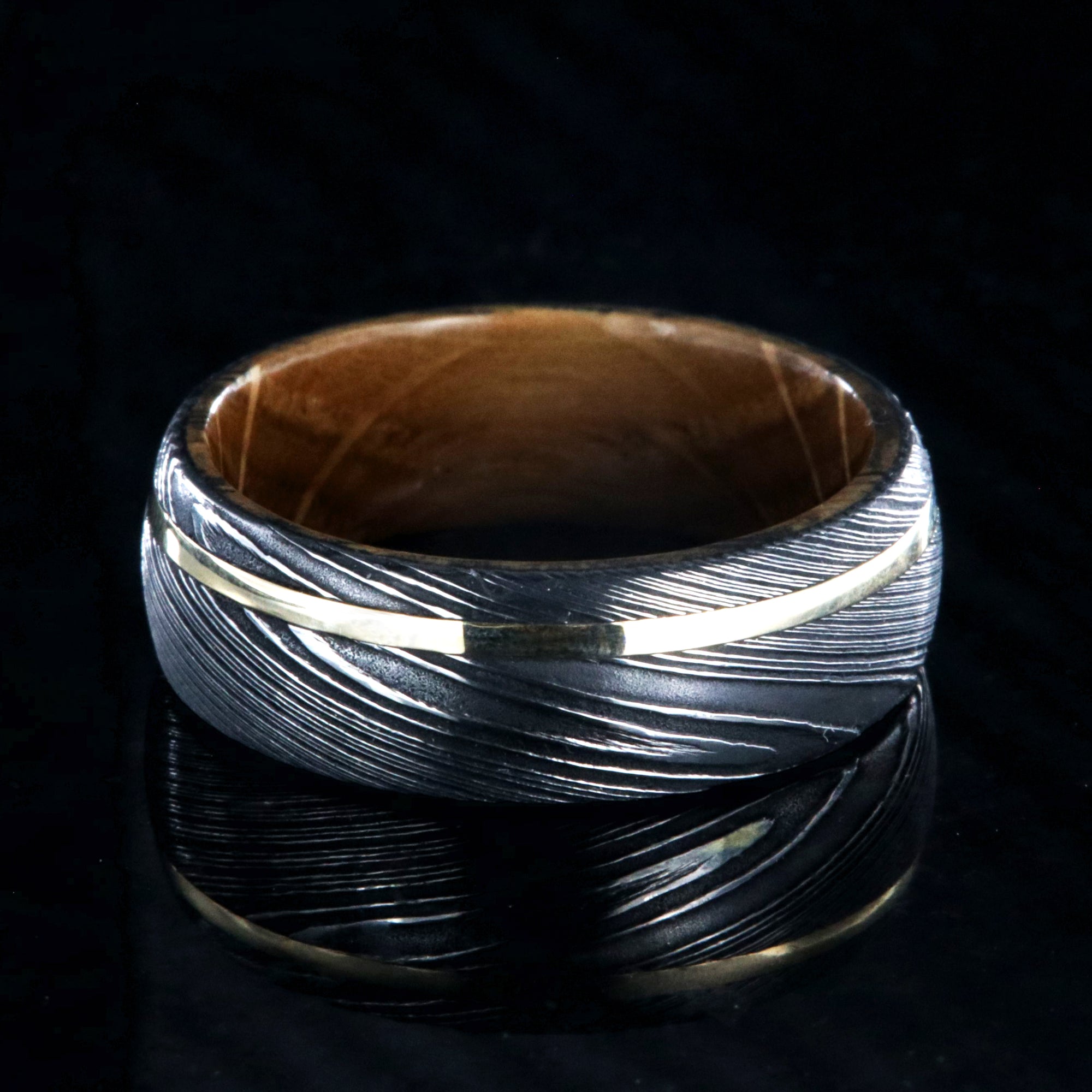 8mm wide Jack Daniel's whiskey barrel sleeve wedding ring set in black Damascus steel with a thin off-centered gold inlay