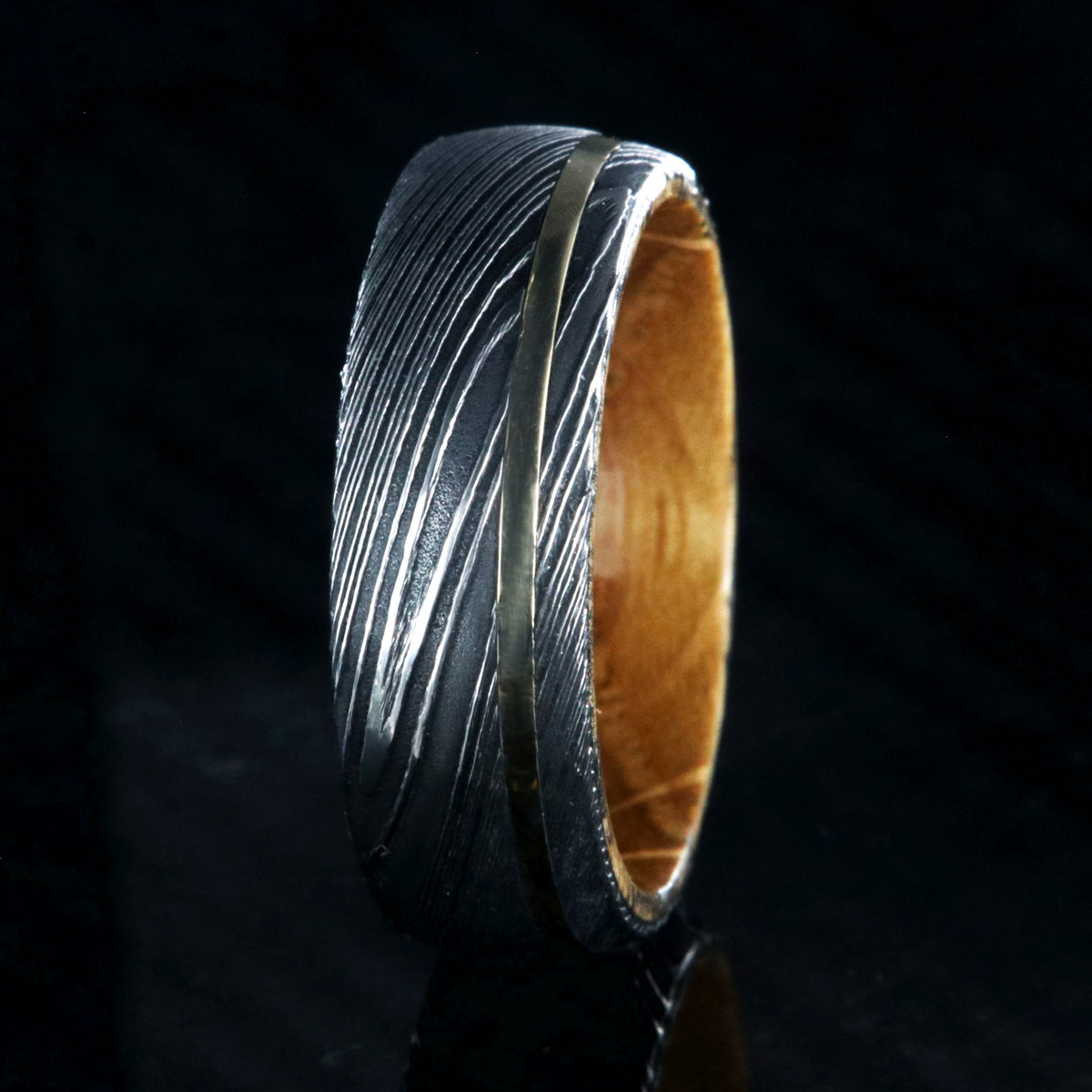 8mm wide Jack Daniel&#39;s whiskey barrel sleeve wedding ring set in black Damascus steel with a thin off-centered gold inlay