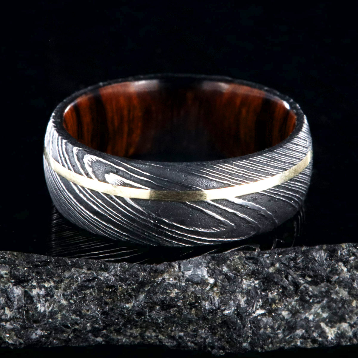 8mm wide black Damascus steel wedding band with rounded profile, an off-center yellow gold inlay, and Arizona ironwood sleeve