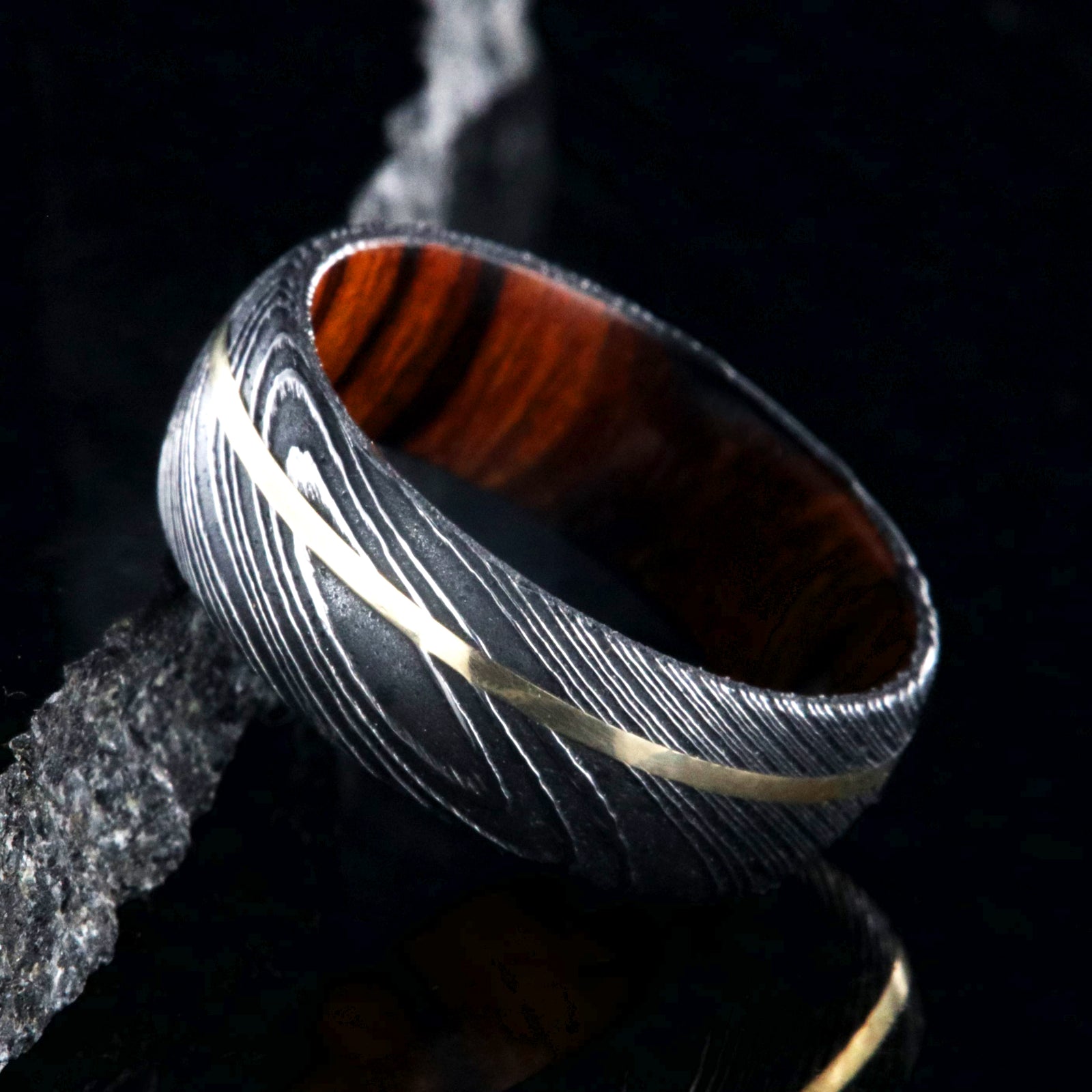 8mm wide black Damascus steel wedding band with rounded profile, an off-center yellow gold inlay, and Arizona ironwood sleeve