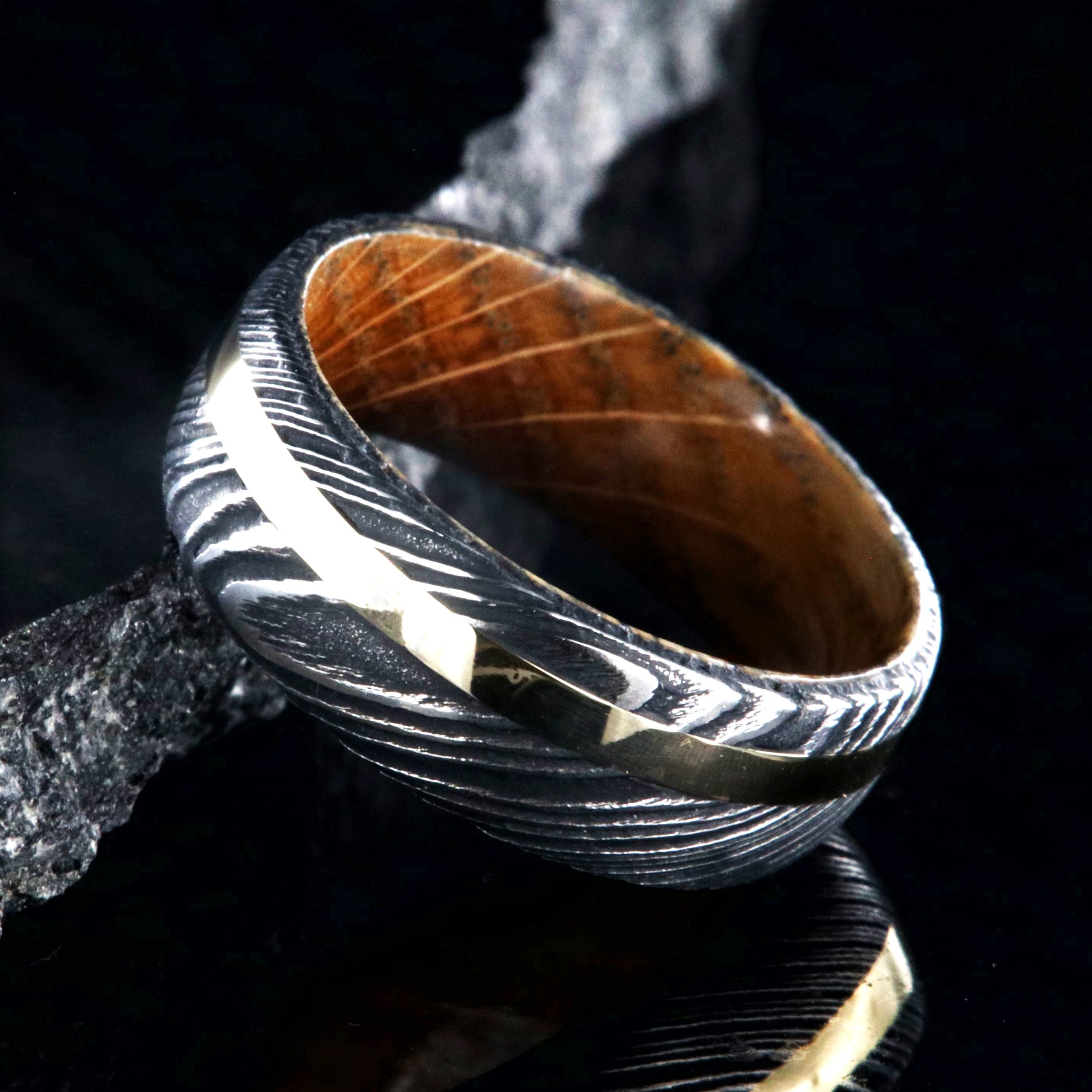 8mm wide black Damascus steel wedding ring with rounded profile, 2mm wide yellow gold inlay and a Jack Daniel's whiskey barrel sleeve