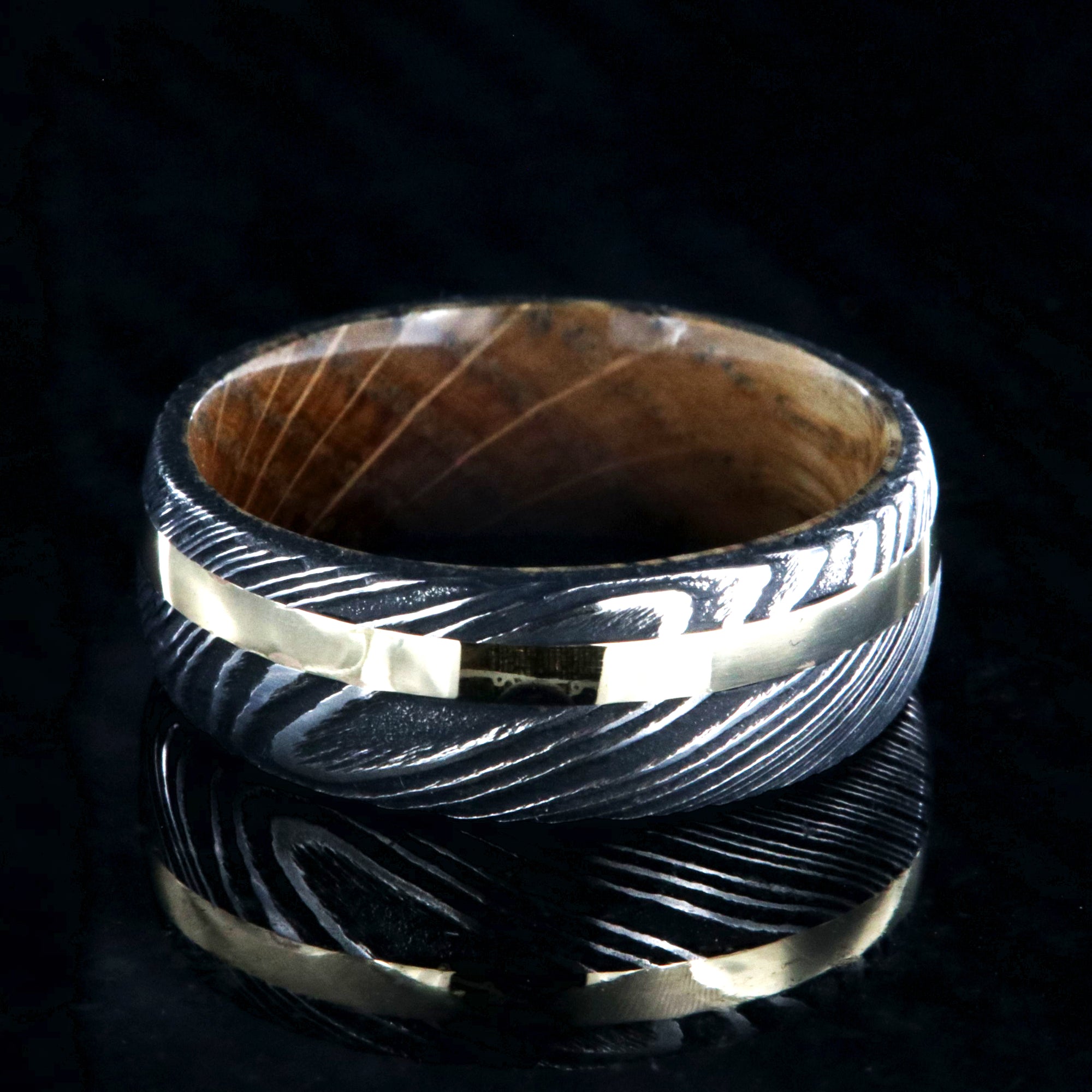 8mm wide black Damascus steel wedding ring with rounded profile, 2mm wide yellow gold inlay and a Jack Daniel's whiskey barrel sleeve