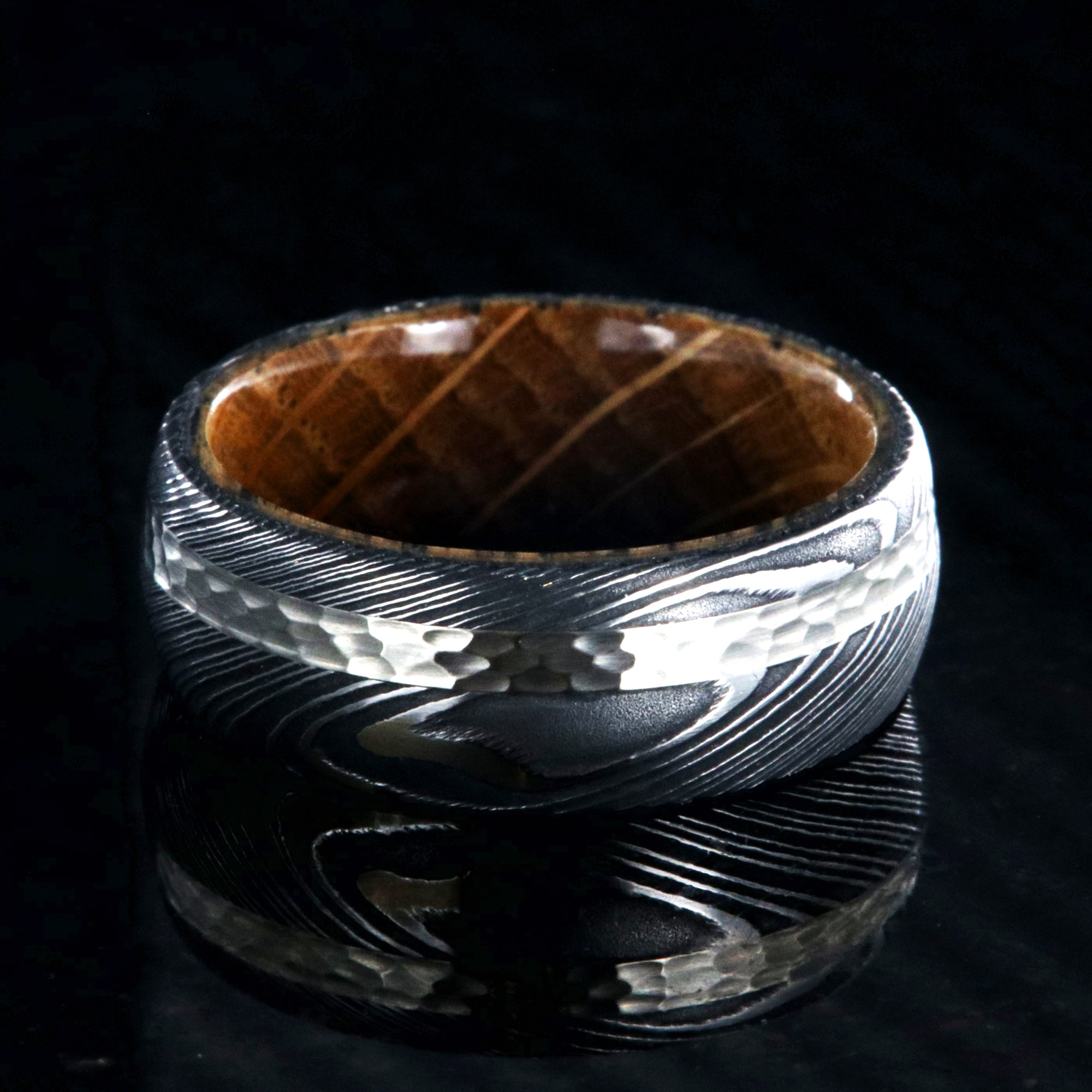 8mm wide black Damascus steel ring with a 2mm wide hammered white gold inlay and a whiskey barrel sleeve