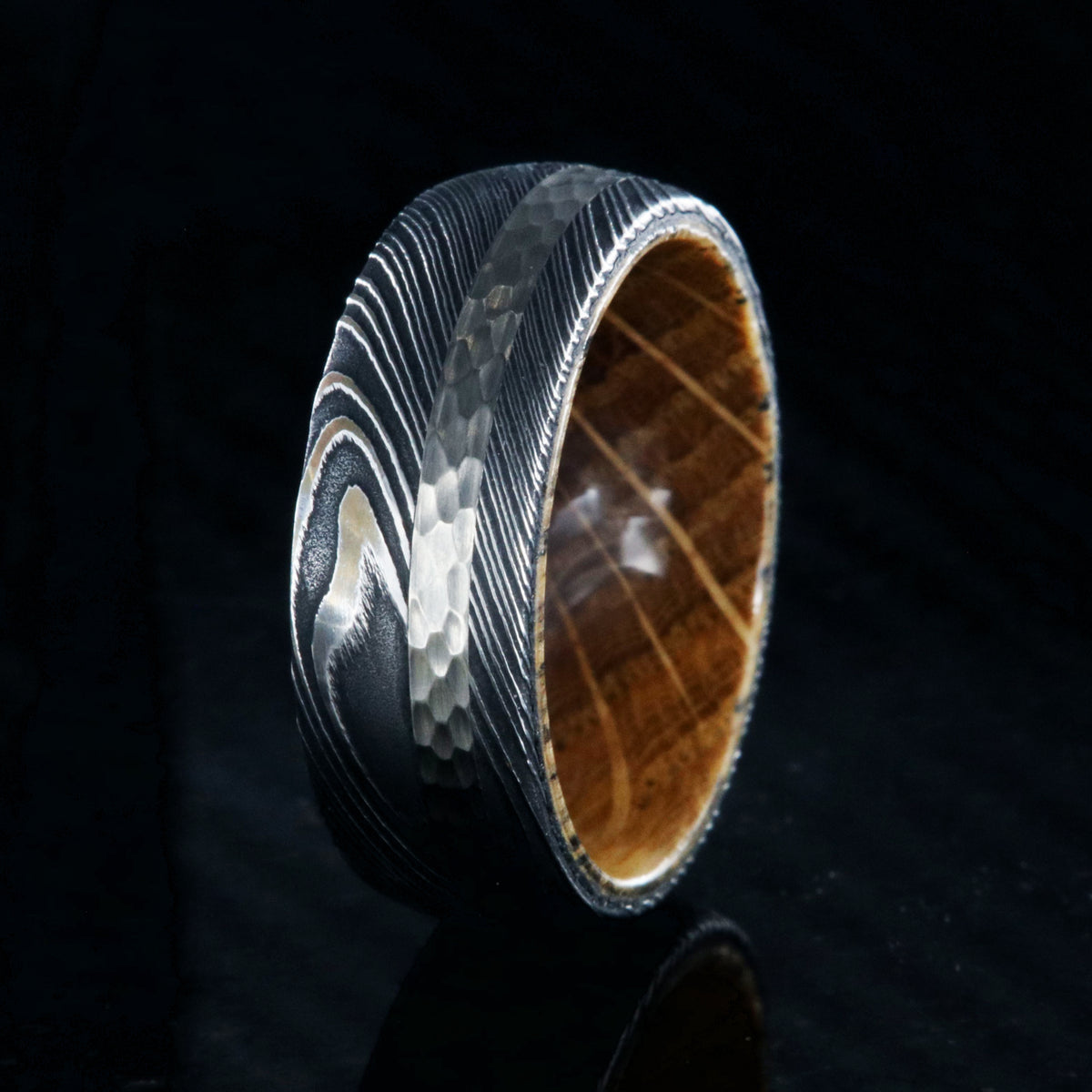 8mm wide black Damascus steel ring with a 2mm wide hammered white gold inlay and a whiskey barrel sleeve