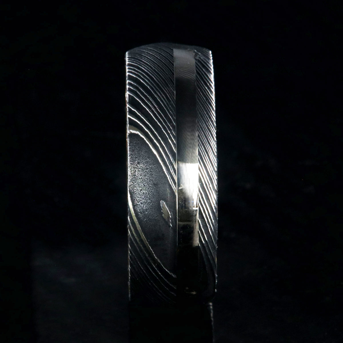 8mm wide mens ring with black Damascus steel and a wide gold off-center inlay and a Jack Daniels whiskey barrel sleeve