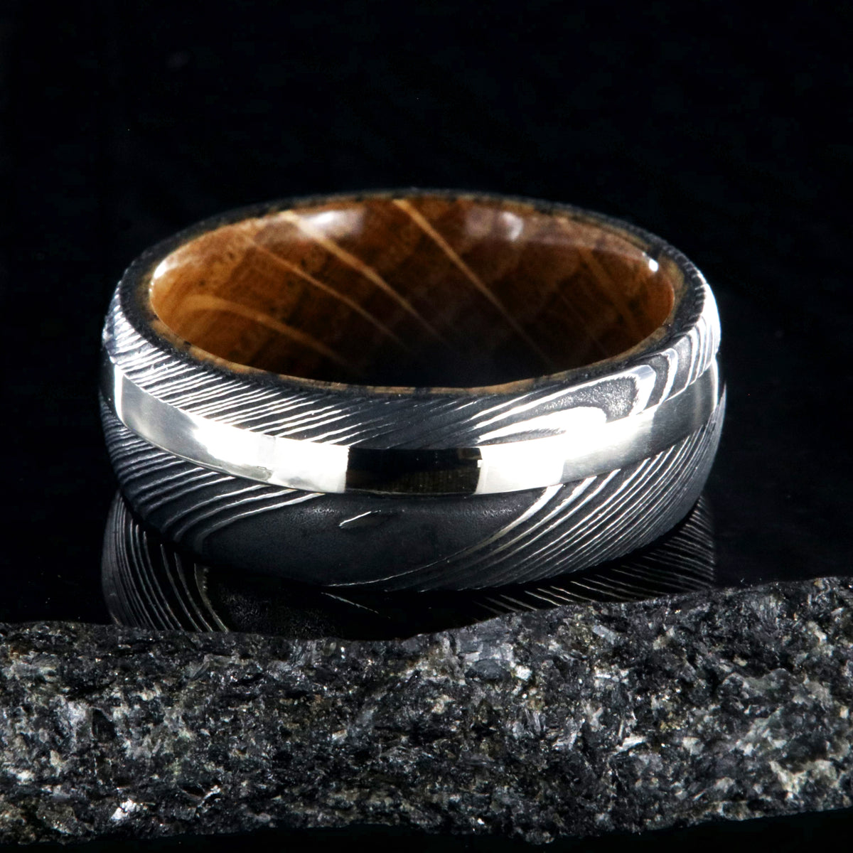 8mm wide mens ring with black Damascus steel and a wide gold off-center inlay and a Jack Daniels whiskey barrel sleeve