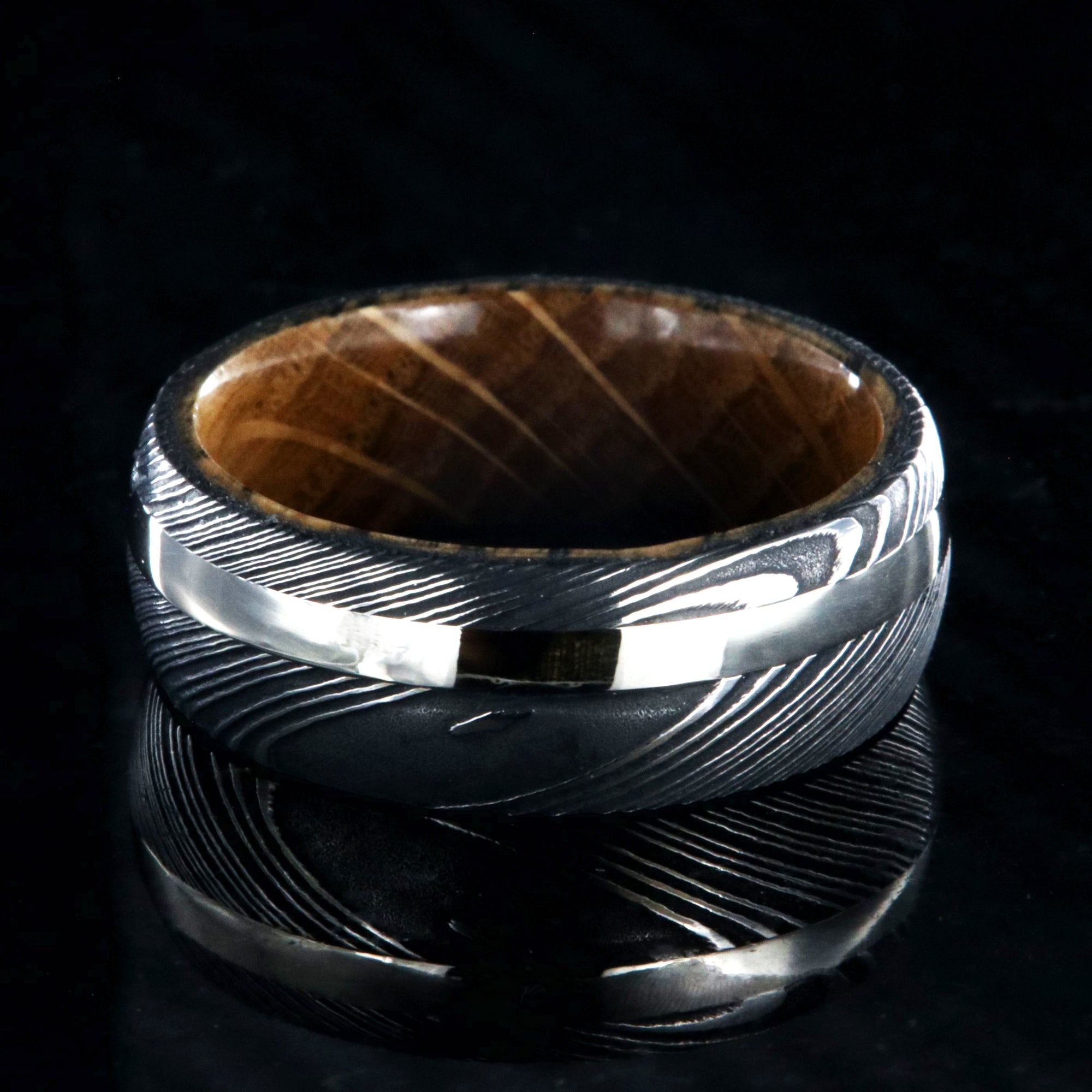 8mm wide mens ring with black Damascus steel and a wide gold off-center inlay and a Jack Daniels whiskey barrel sleeve