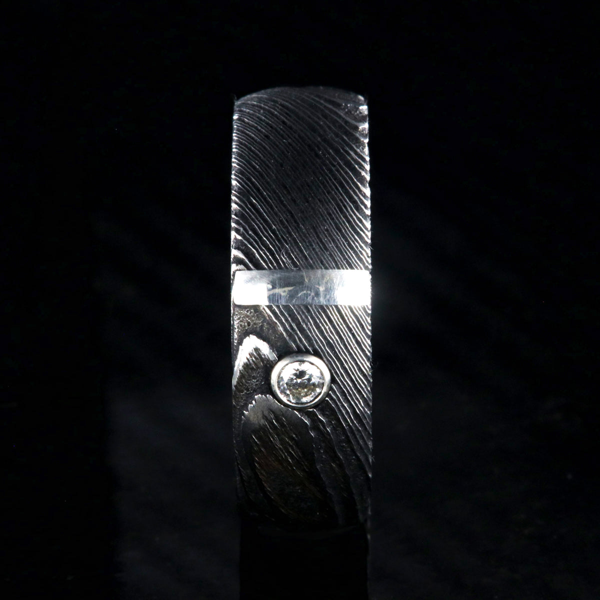 8mm wide black Damascus steel ring with polished inside, rounded profile, a vertical sterling silver inlay, and bezel set diamond