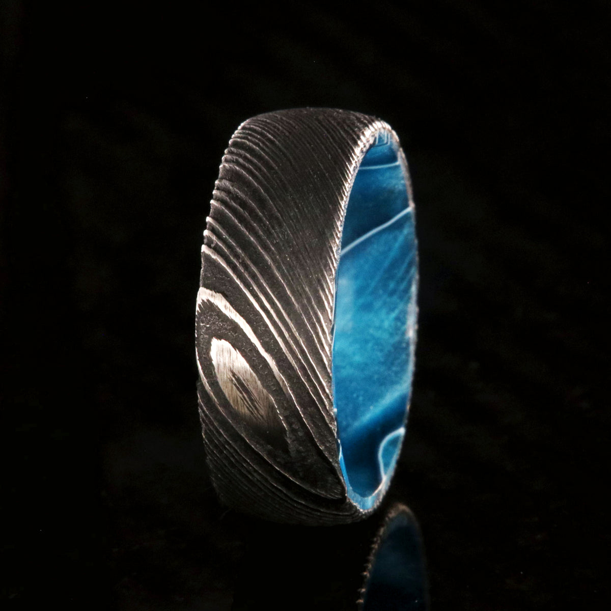7mm wide black Damascus steel wedding band with an ocean blue sleeve and rounded profile